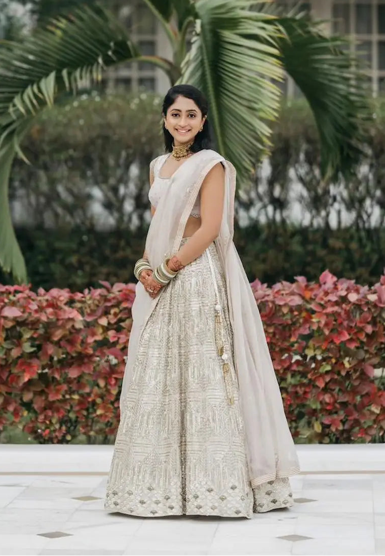 Woman in a white saree standing in front of a palm tree and greenery