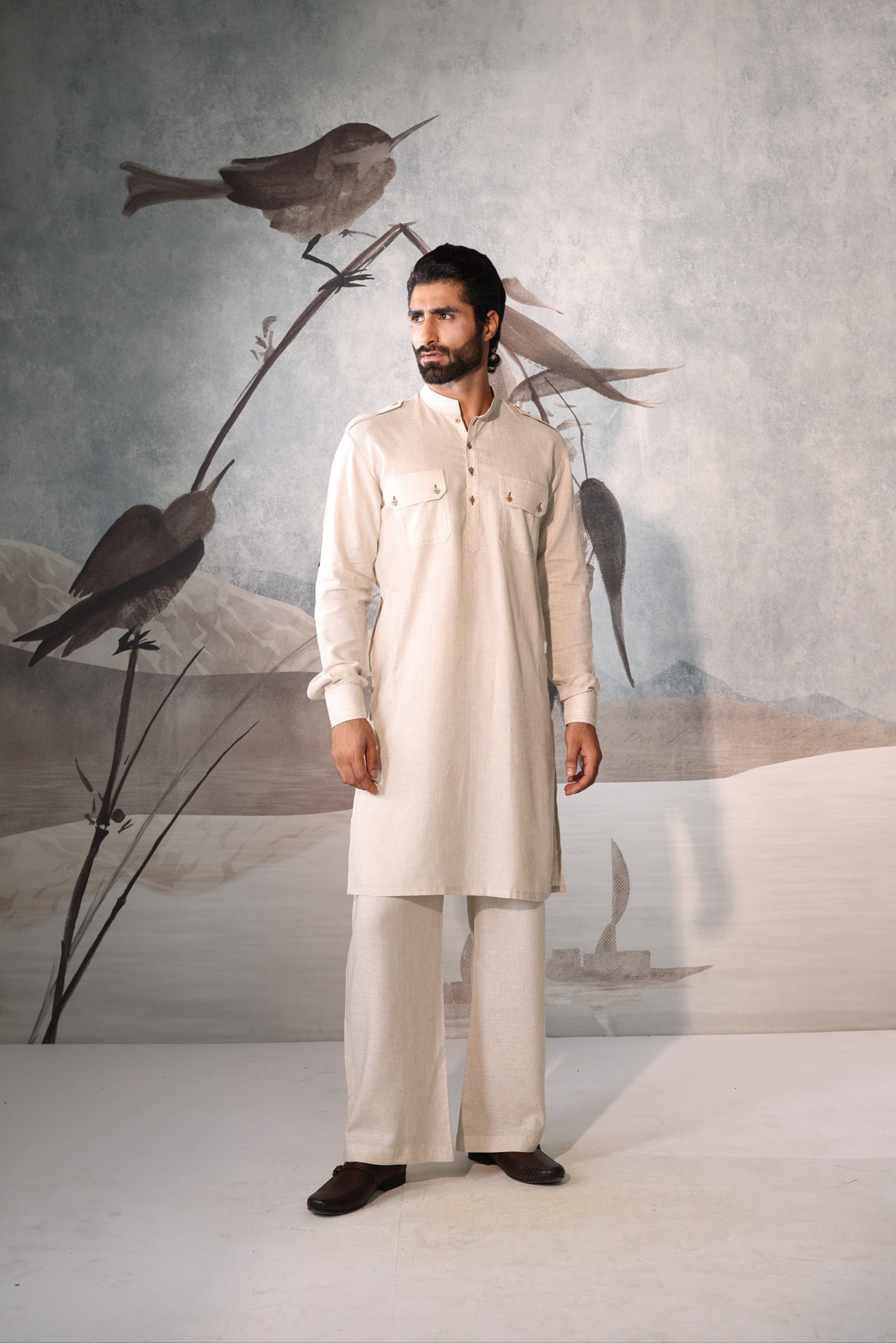 Man wearing a white traditional outfit standing in front of a wall with bird artwork.
