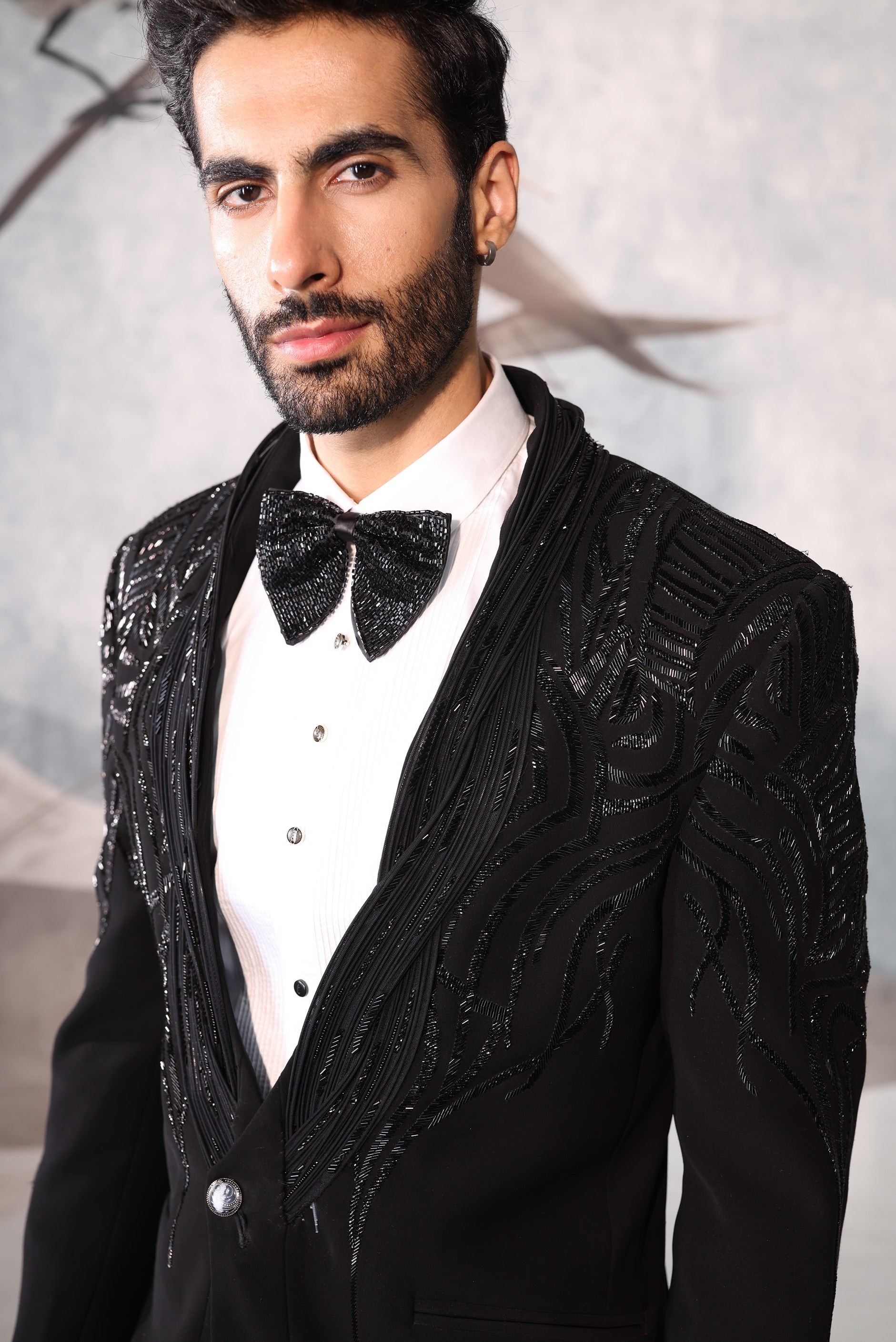 Man wearing a black sequined tuxedo with a bow tie against a neutral background