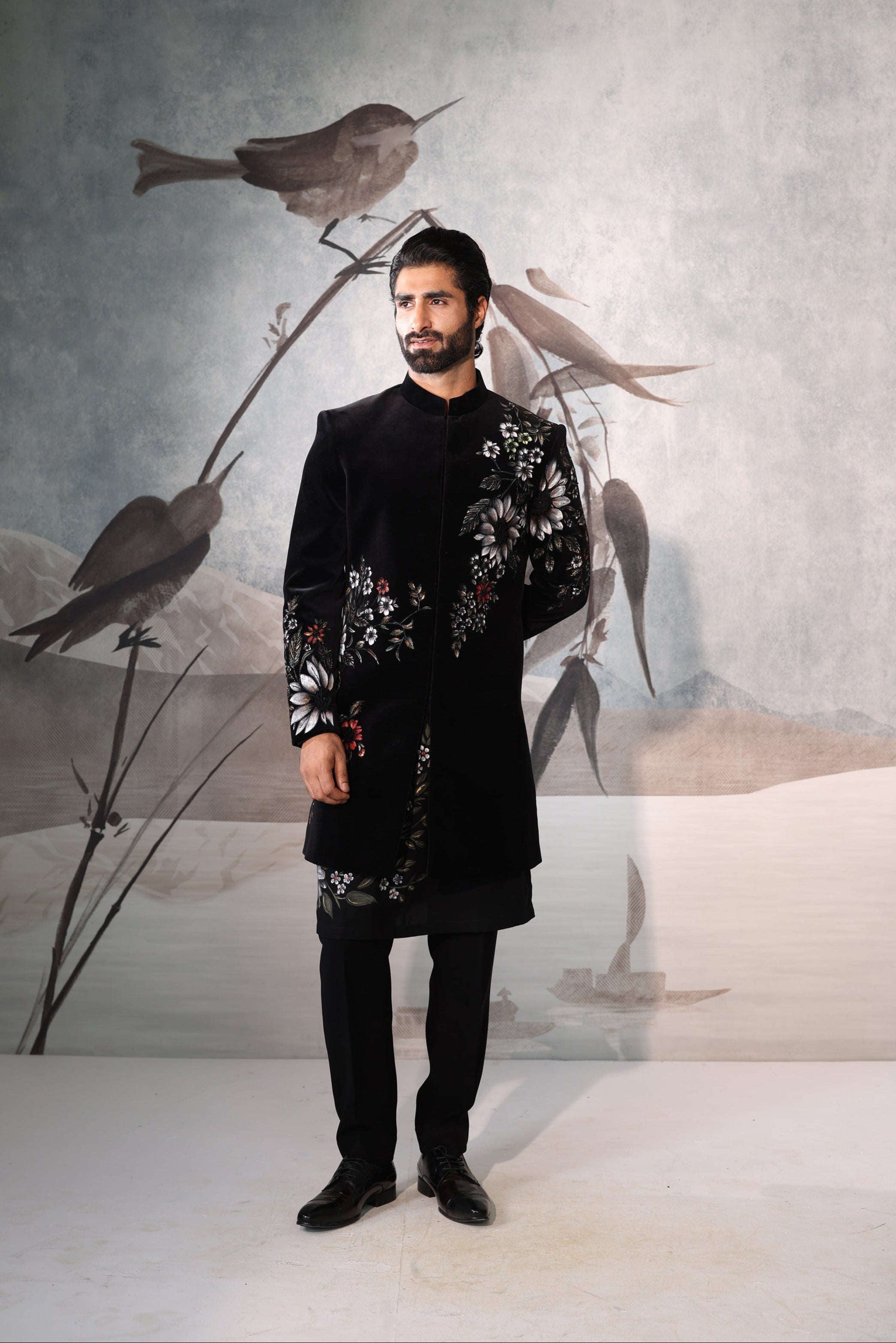 Man in a black traditional outfit standing in front of a wall with bird artwork