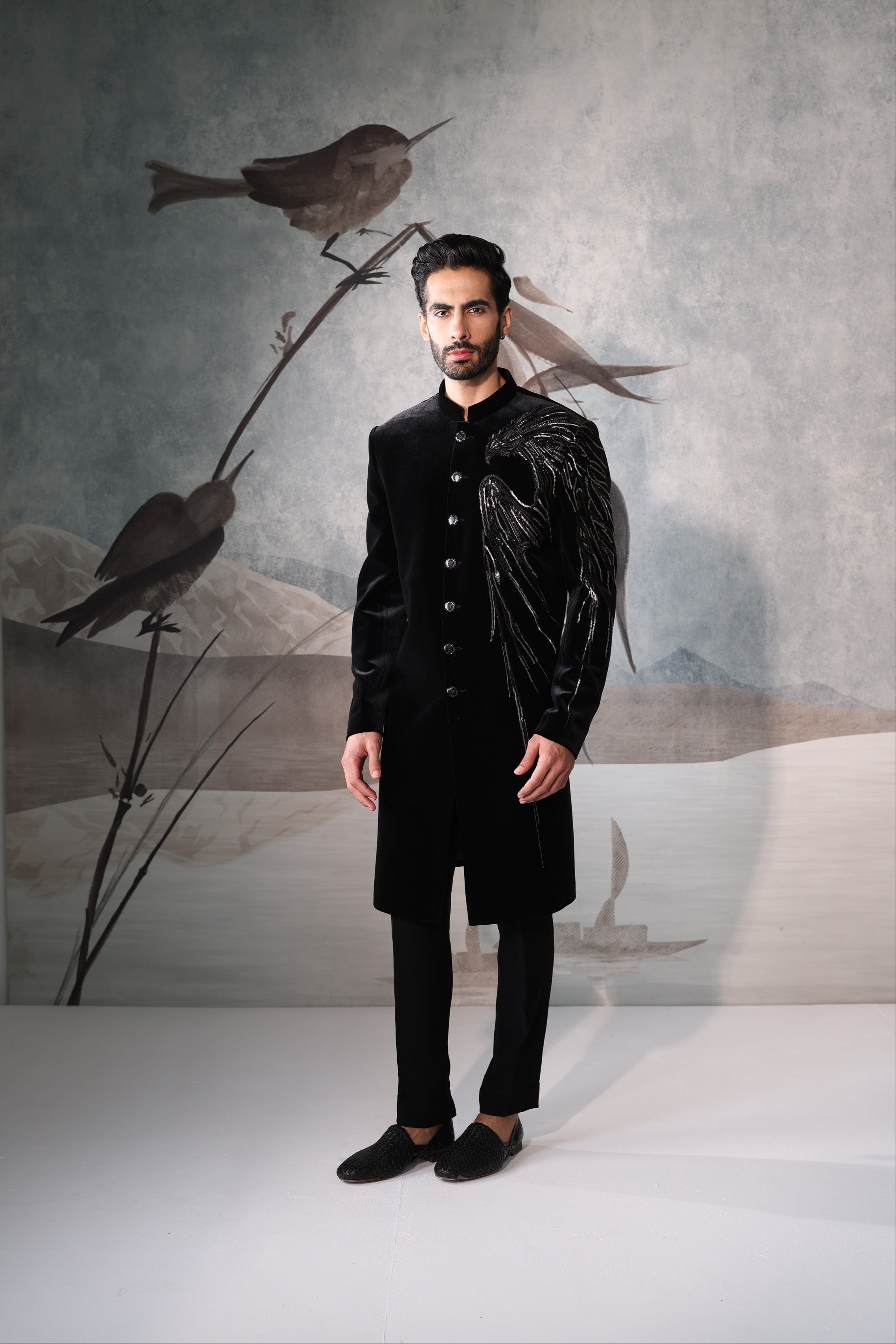 Man in a black suit standing in front of a wall with bird artwork