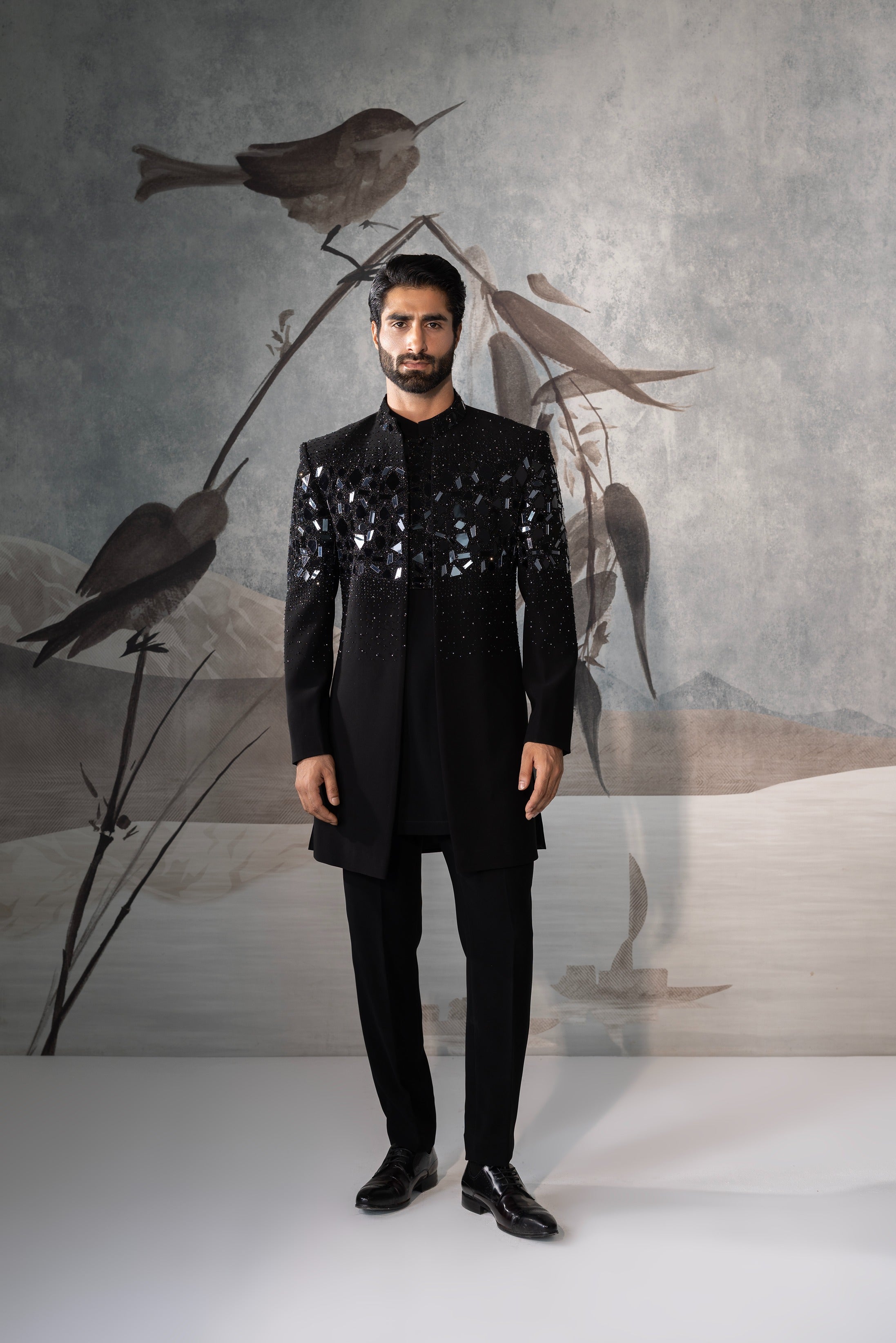 Man in a black outfit standing against a backdrop with stylized bird illustrations.