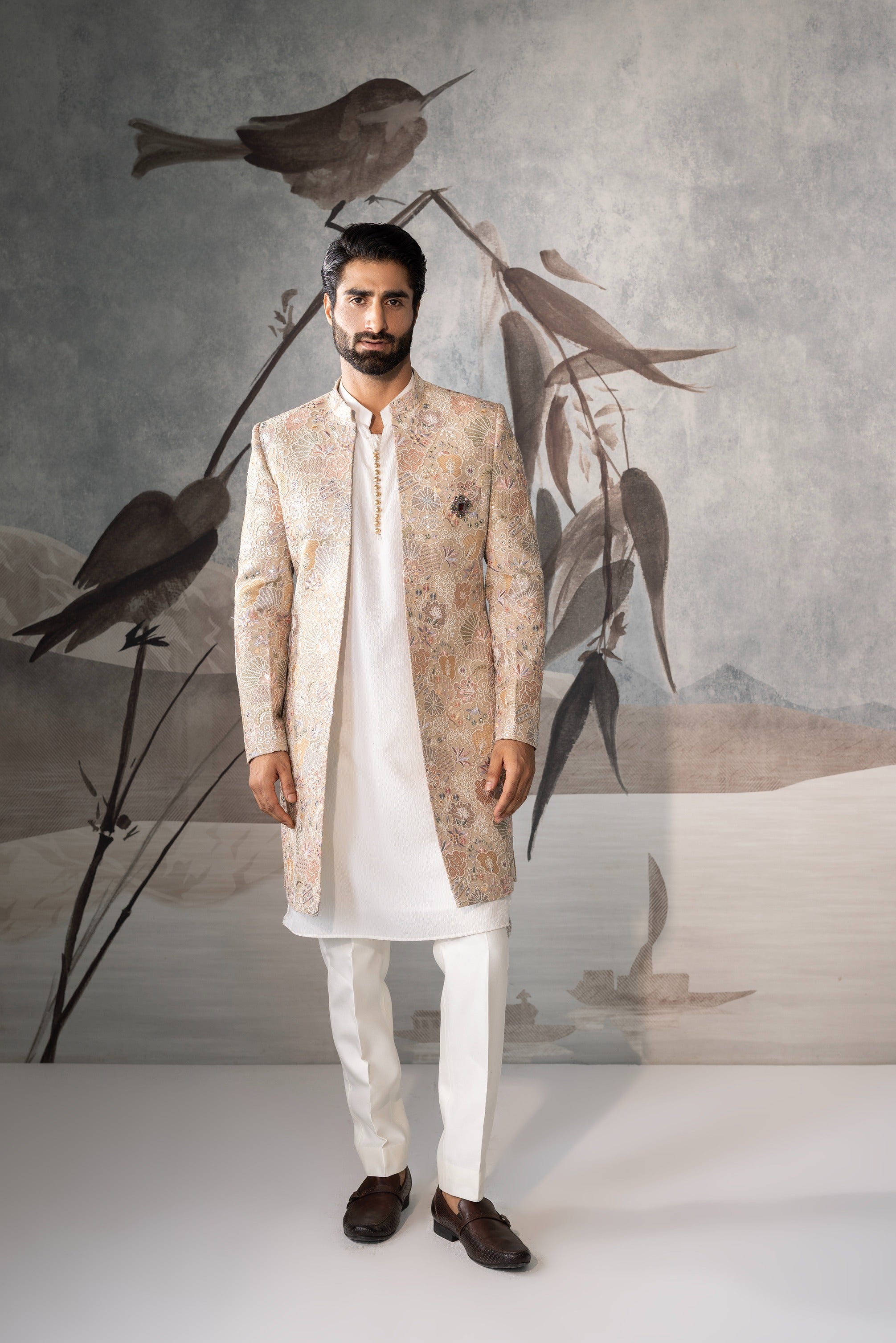 Man wearing a traditional outfit with a decorative background featuring birds.