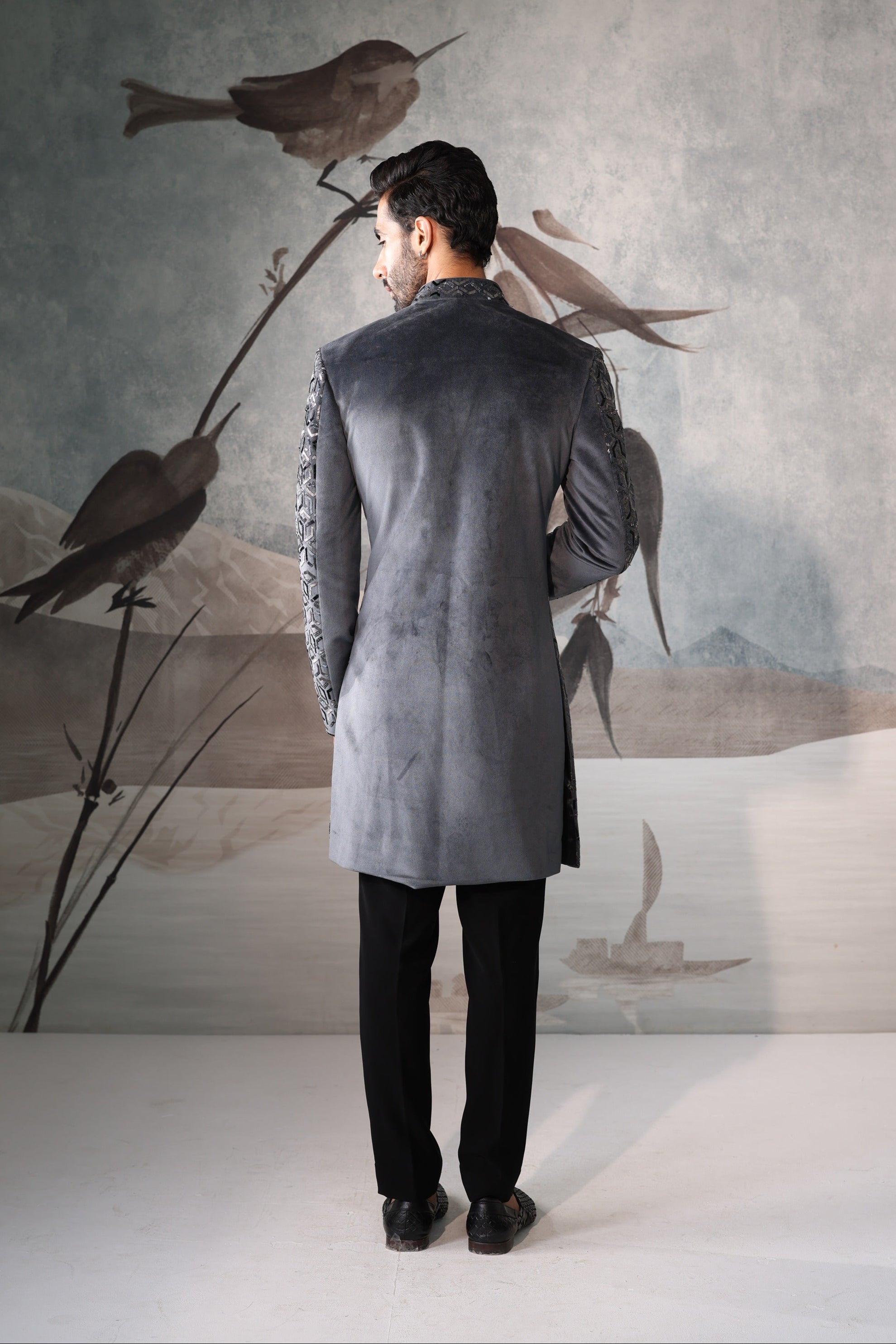 Man in a gray coat standing in front of a wall with bird artwork