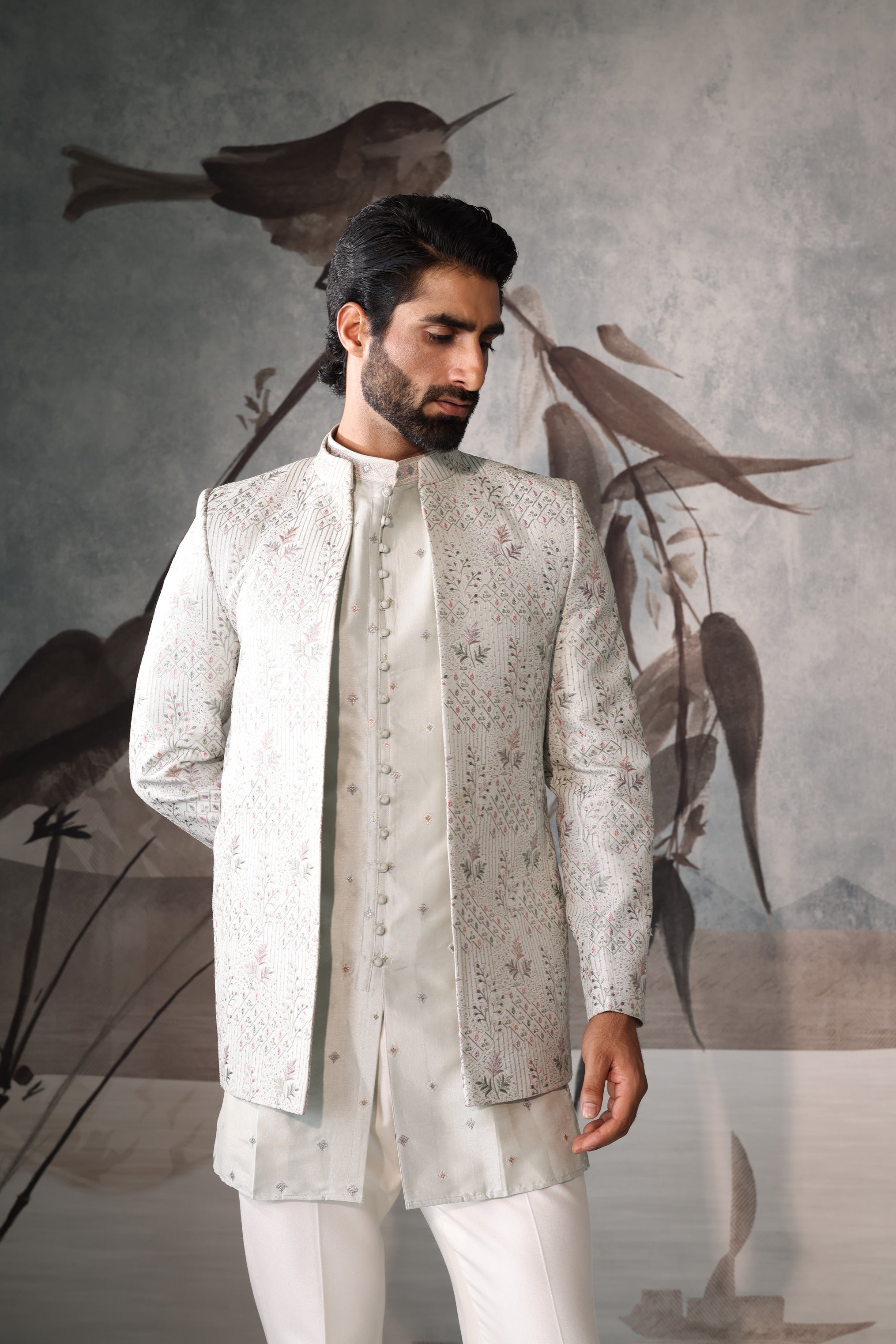 Man wearing a traditional embroidered outfit with a stylized bird illustration in the background