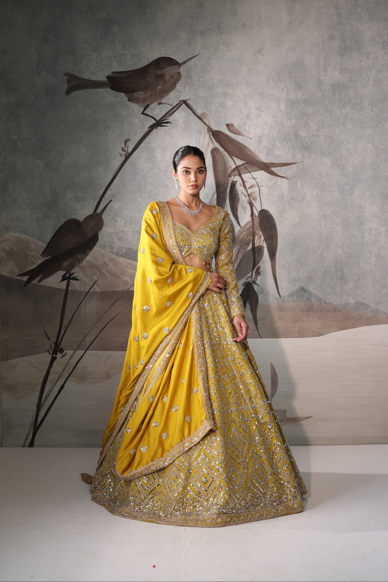 Woman in a yellow and gold traditional outfit standing against a wall with bird artwork.