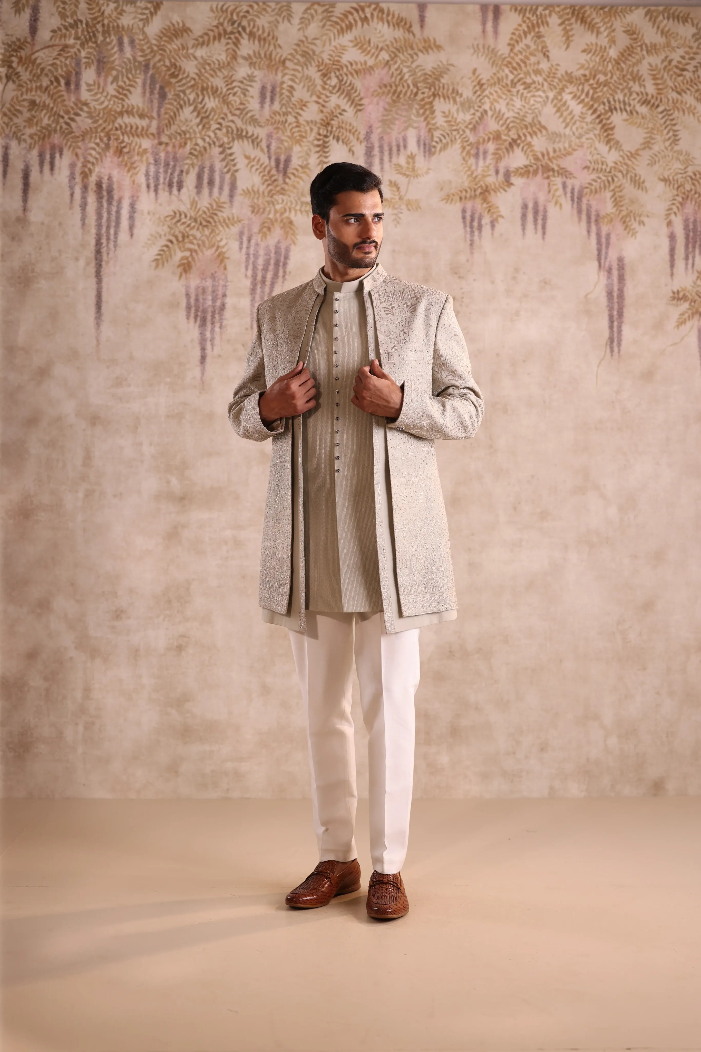 Man wearing a traditional outfit with a textured wall background