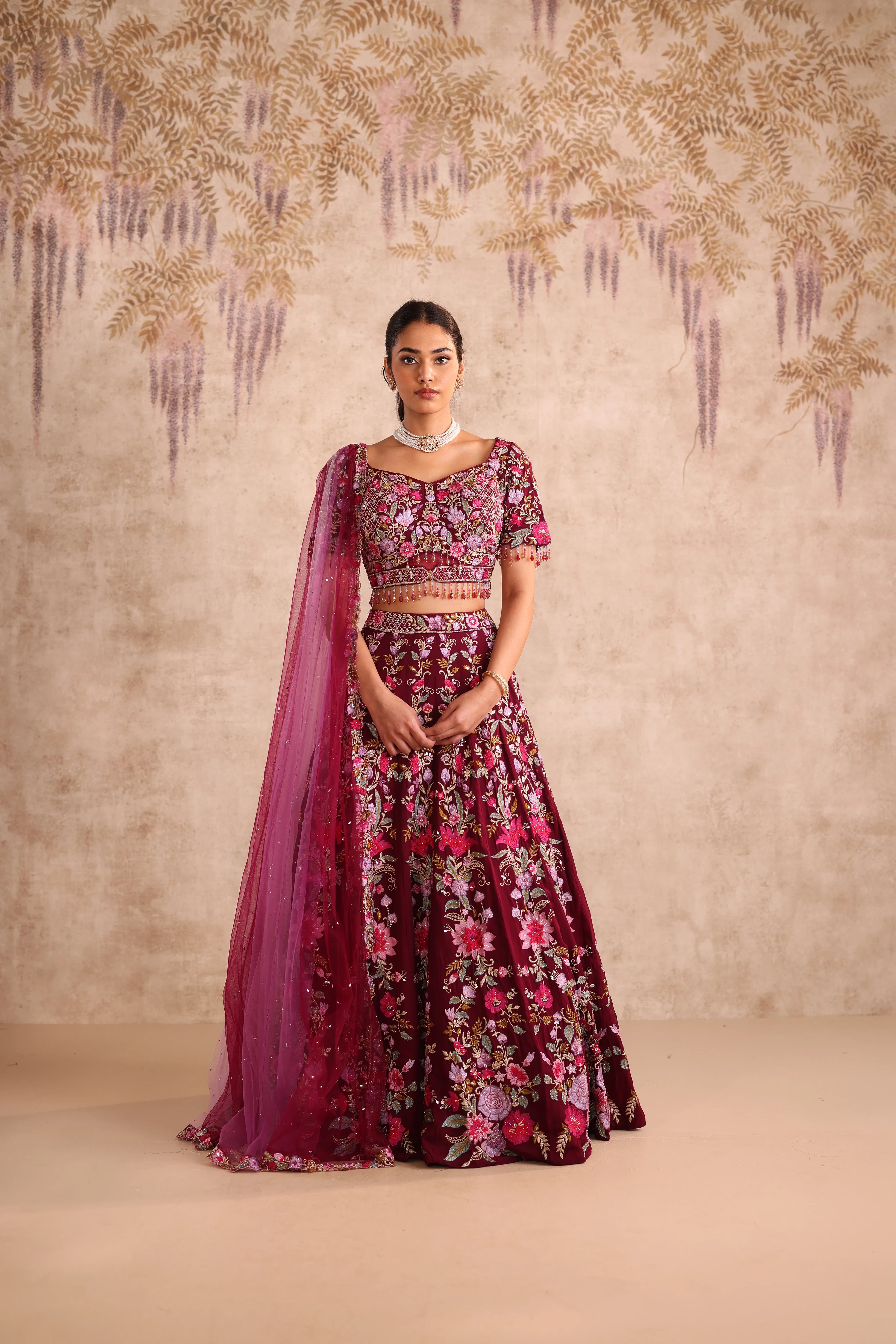 Woman wearing a floral dress with a pink dupatta against a decorative wall.