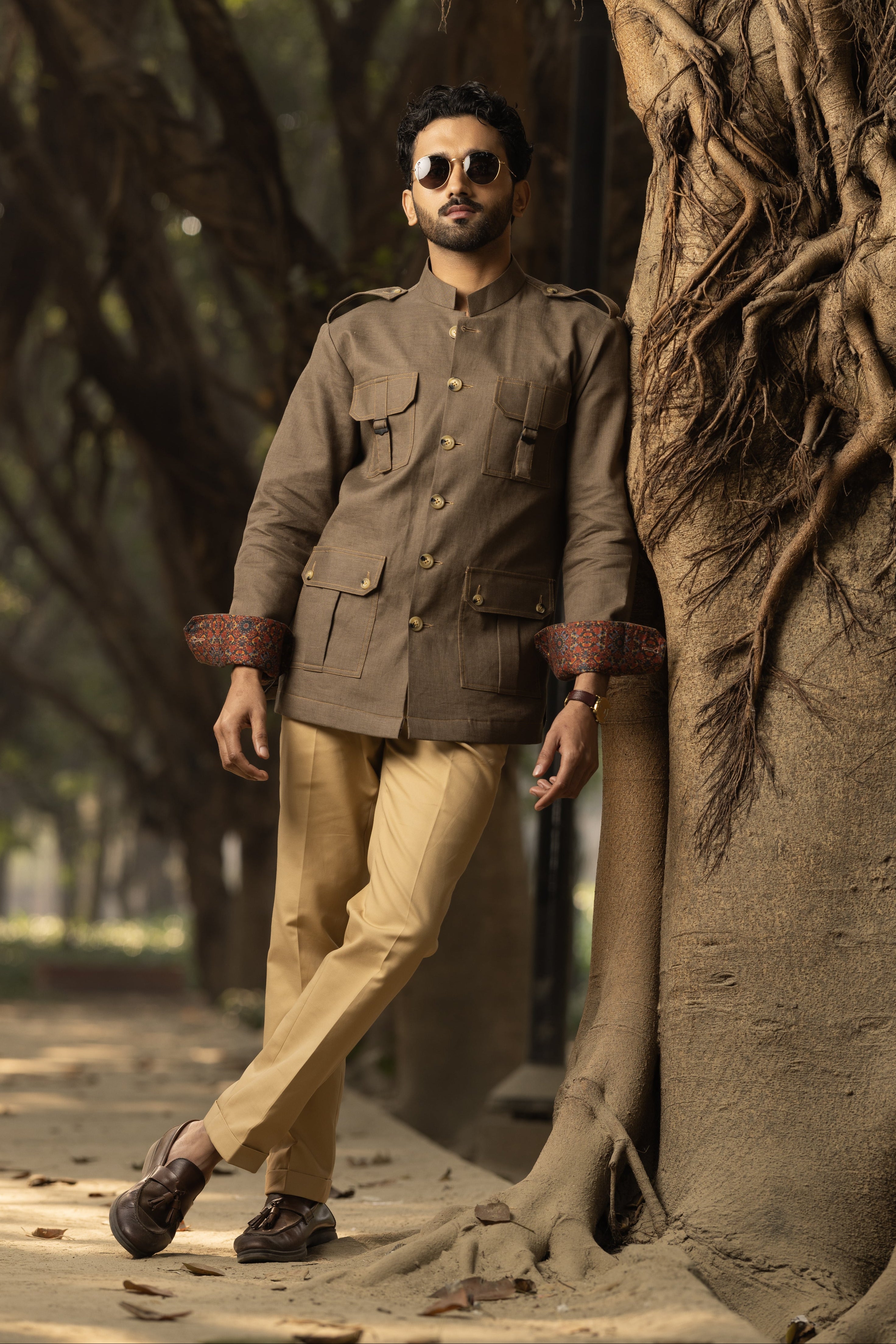 A person wearing a brown linen safari shirt with a structured collar and tailored fit, standing next to a large tree.