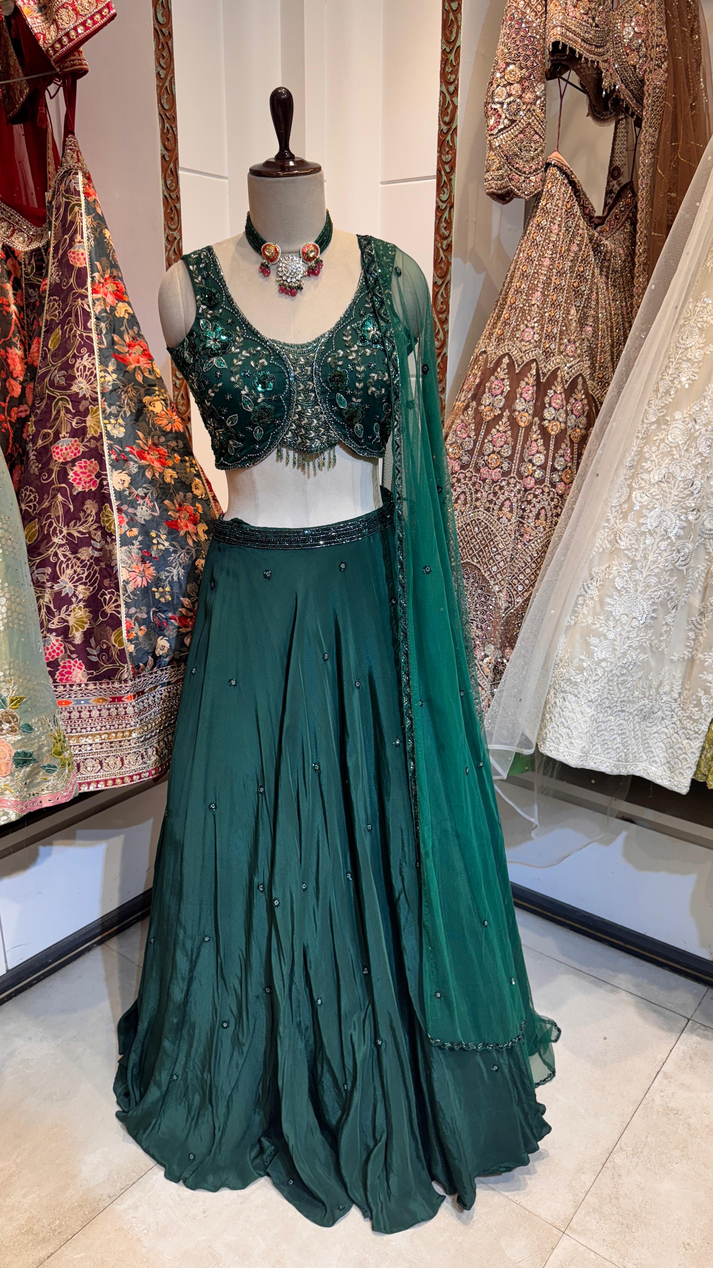 A green lehenga with sequins and embroidery, displayed on a mannequin, paired with a matching blouse and a sheer dupatta with sequin-embroidered borders.