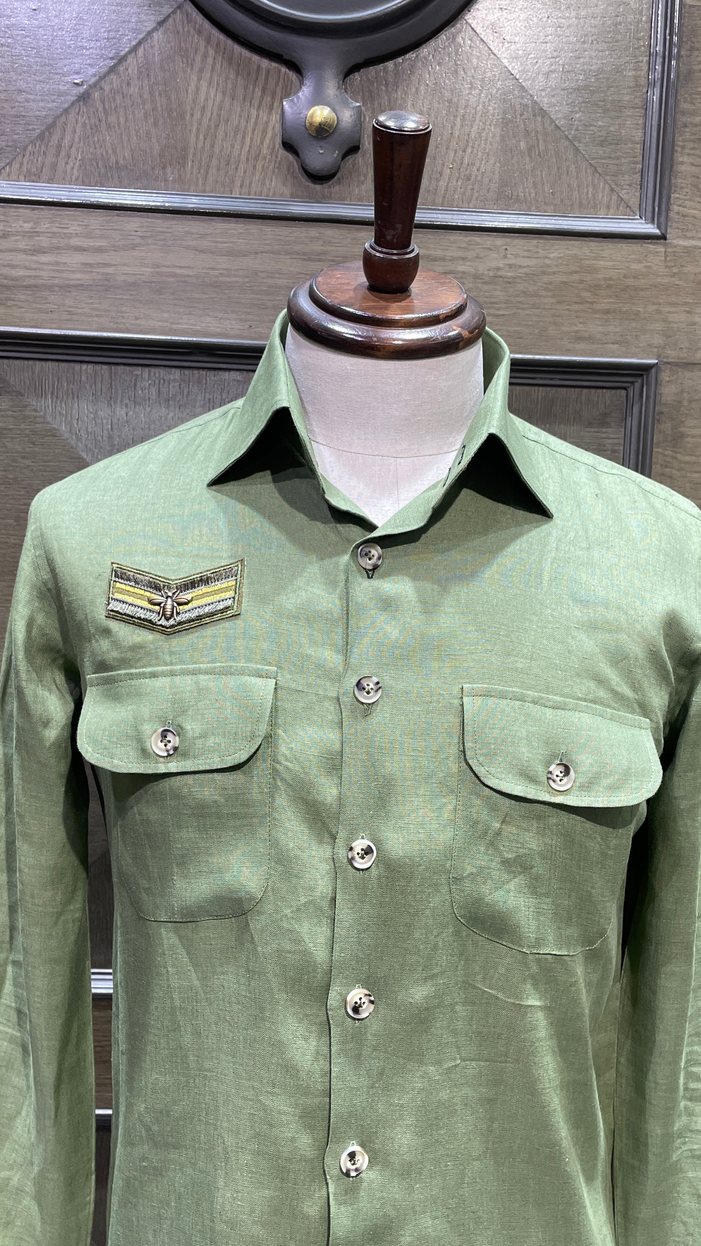 Green shirt on a mannequin with decorative buttons against a neutral background