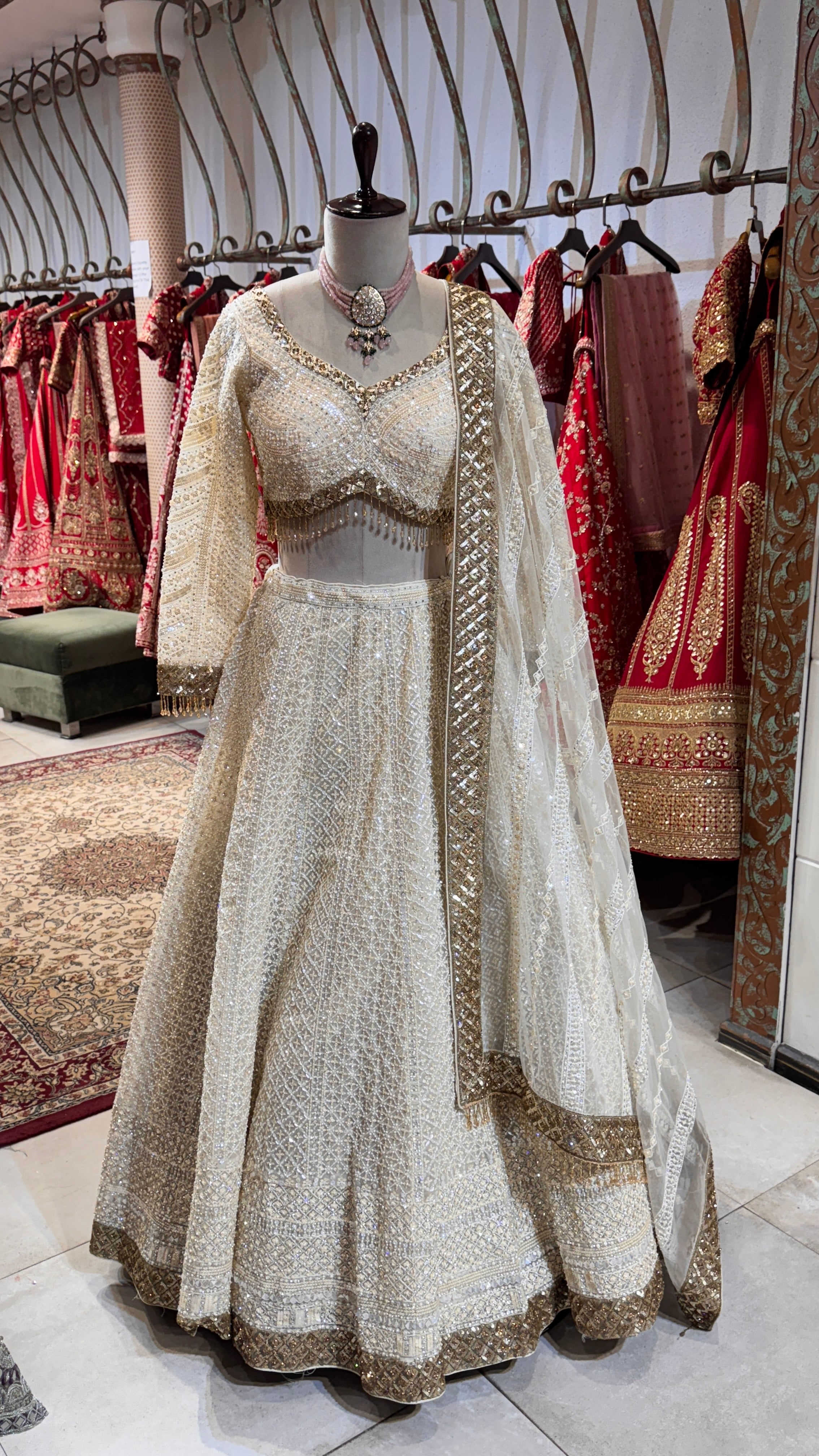 A mannequin displaying a white lehenga with intricate embroidery, paired with a matching blouse and a sheer dupatta with embroidered borders.