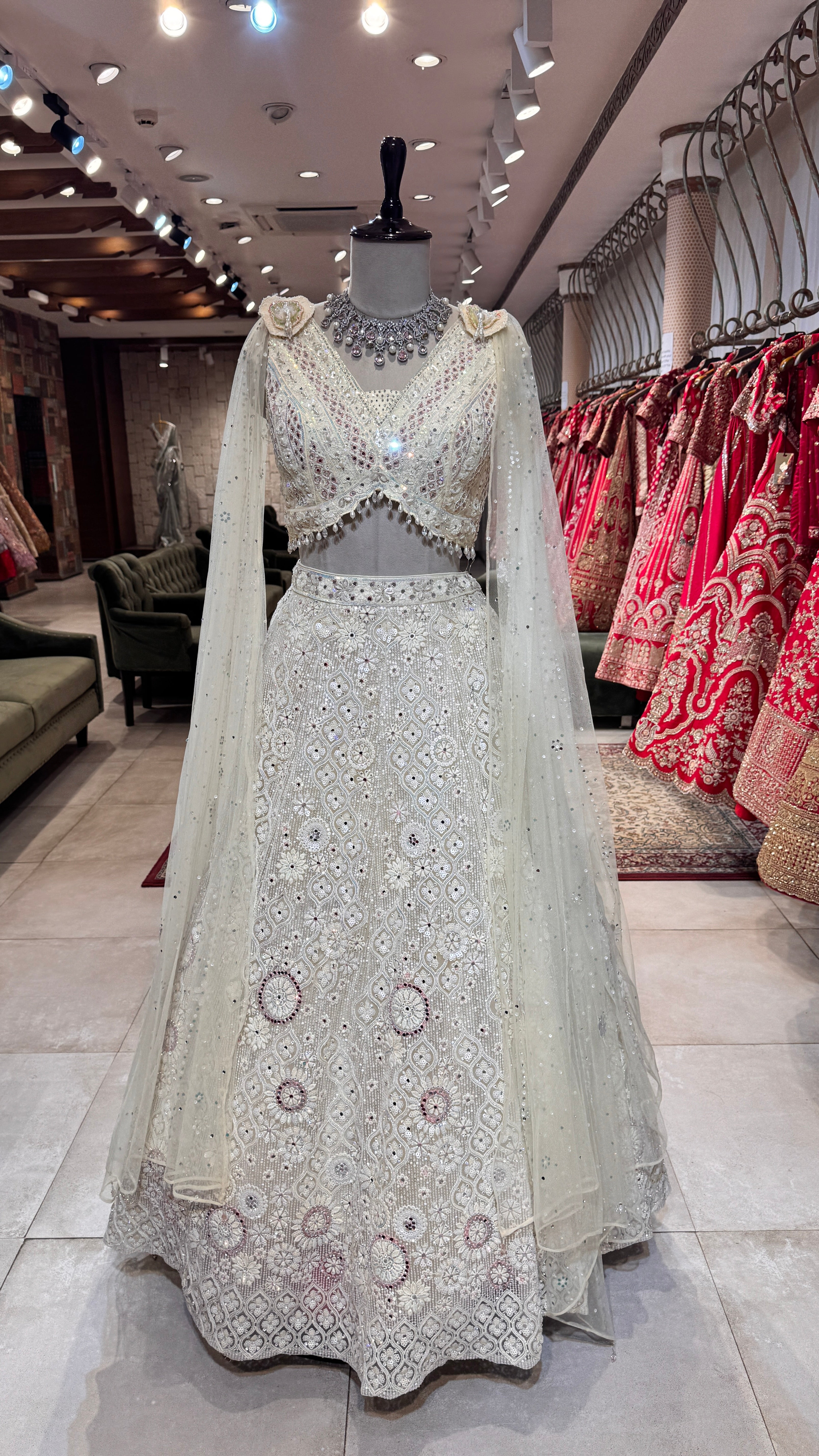 A mannequin displaying a white floral lehenga with embroidery, paired with a matching blouse and a sheer dupatta with floral details.