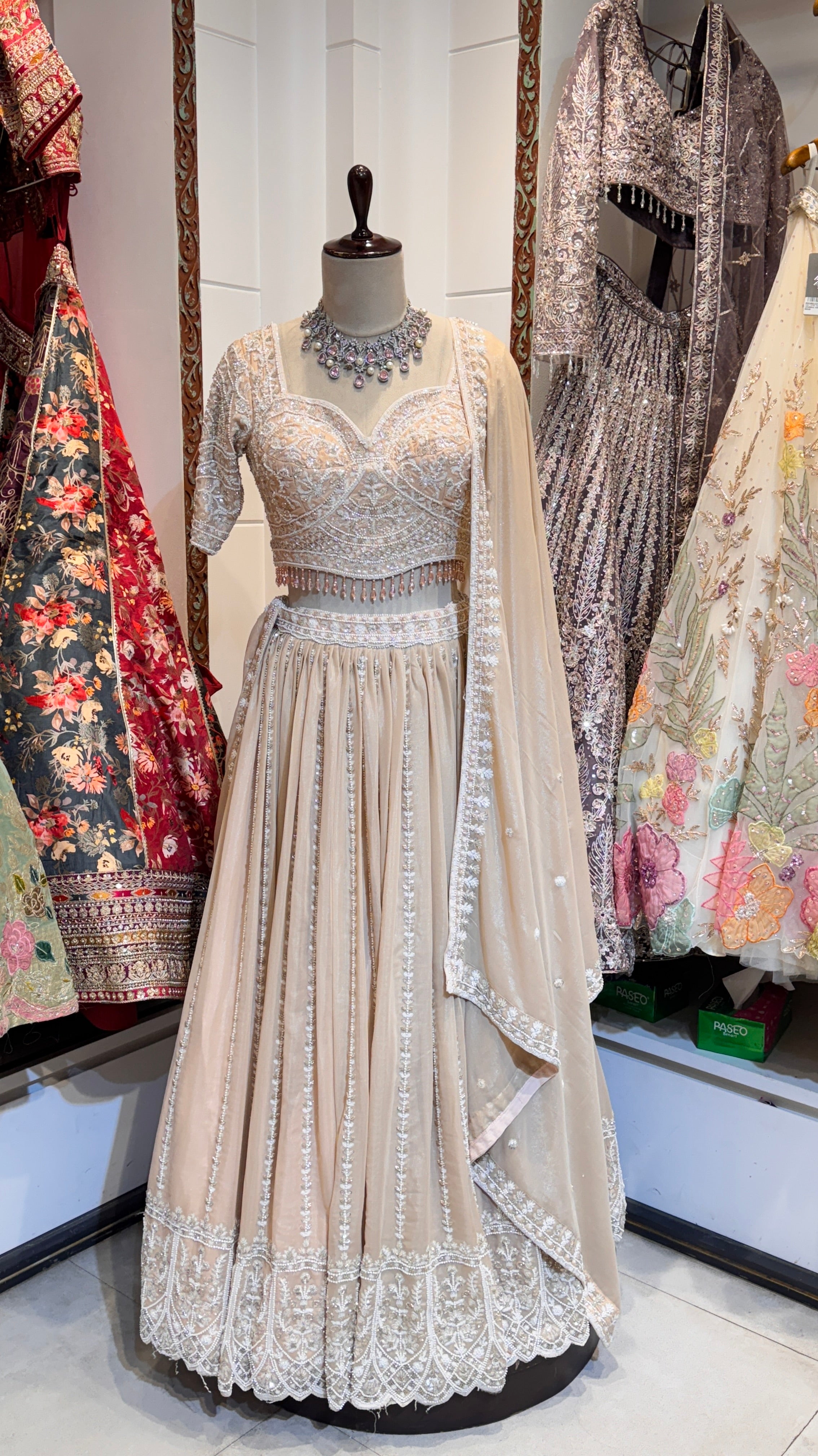 A peach-colored lehenga with embroidery and subtle embellishments, displayed on a mannequin, paired with a matching blouse and a sheer dupatta.