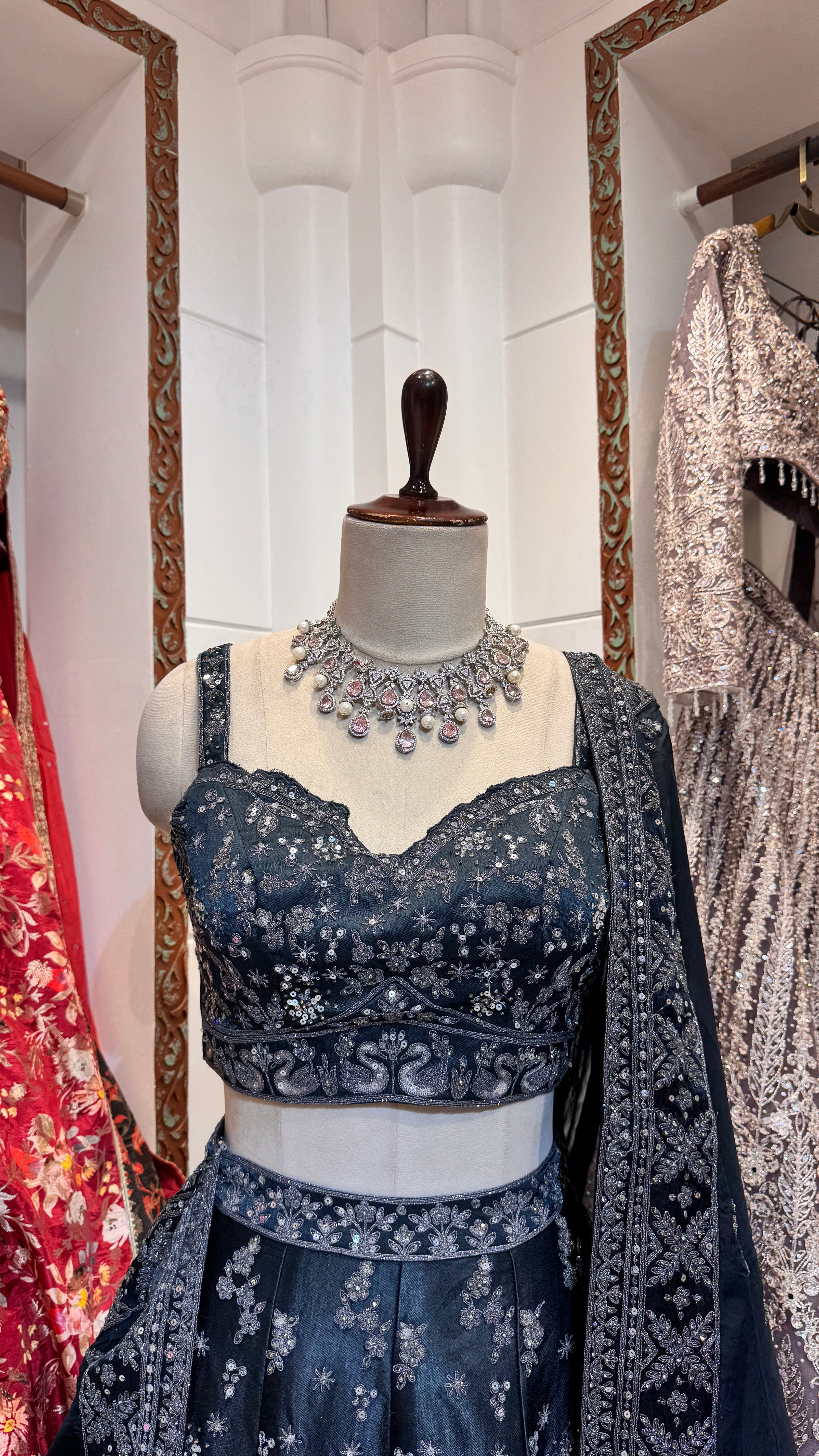 A mannequin displaying a deep blue lehenga with intricate silver embroidery and a matching blouse, paired with a dupatta with silver-embroidered borders.