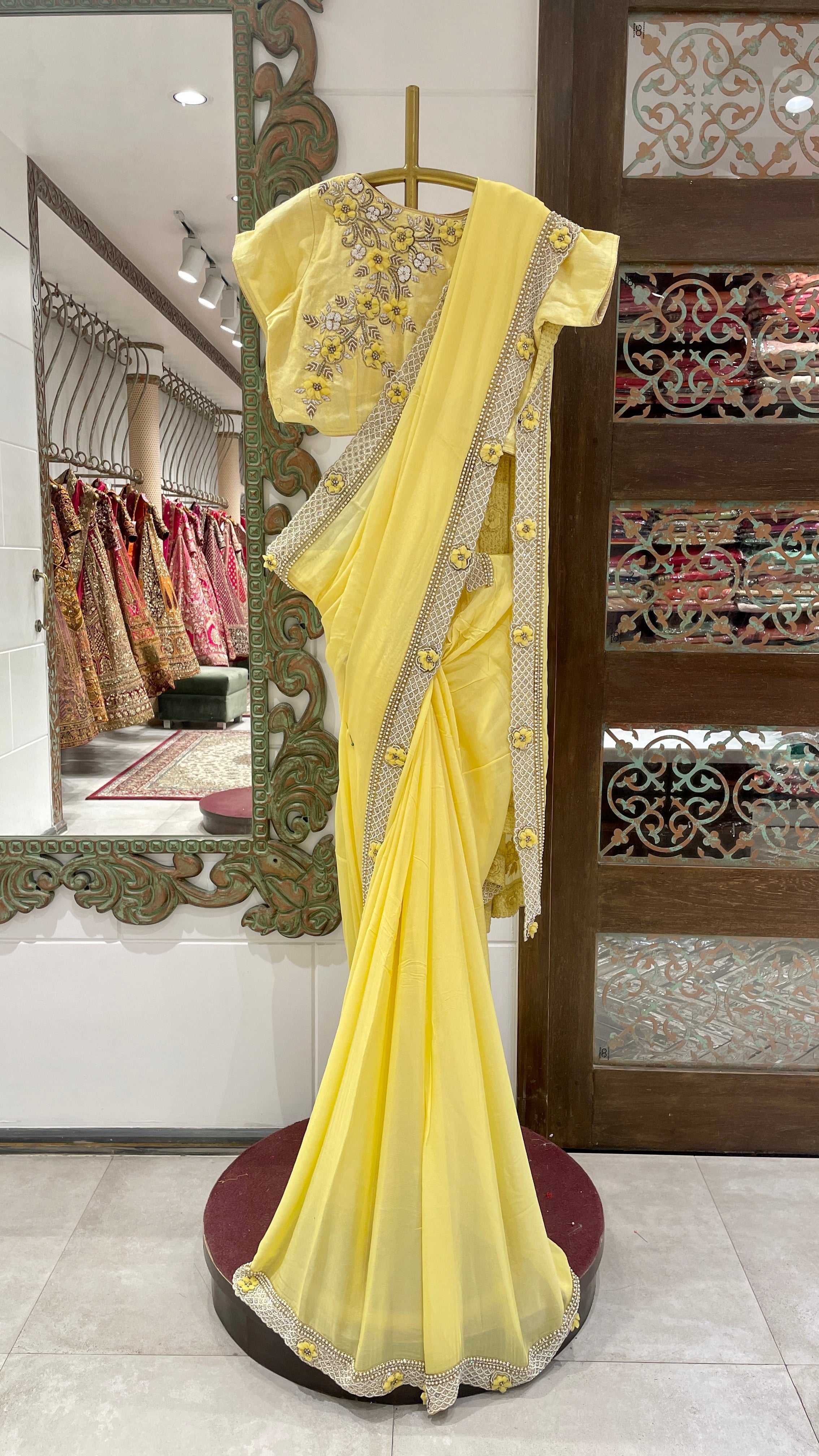 A yellow georgette saree with floral motifs displayed on a mannequin in a store with elaborate floral patterns and a bright yellow color.