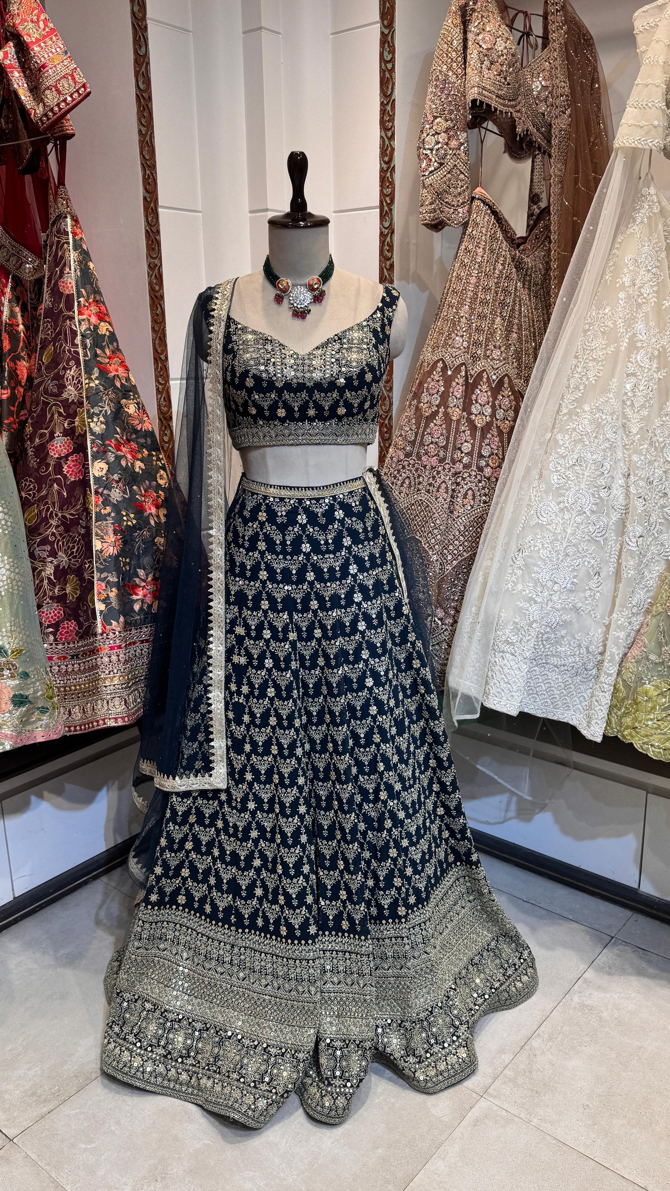 A mannequin displaying a rich dark green lehenga with intricate embroidery and a matching blouse, paired with a sheer dupatta highlighted with embroidered borders.