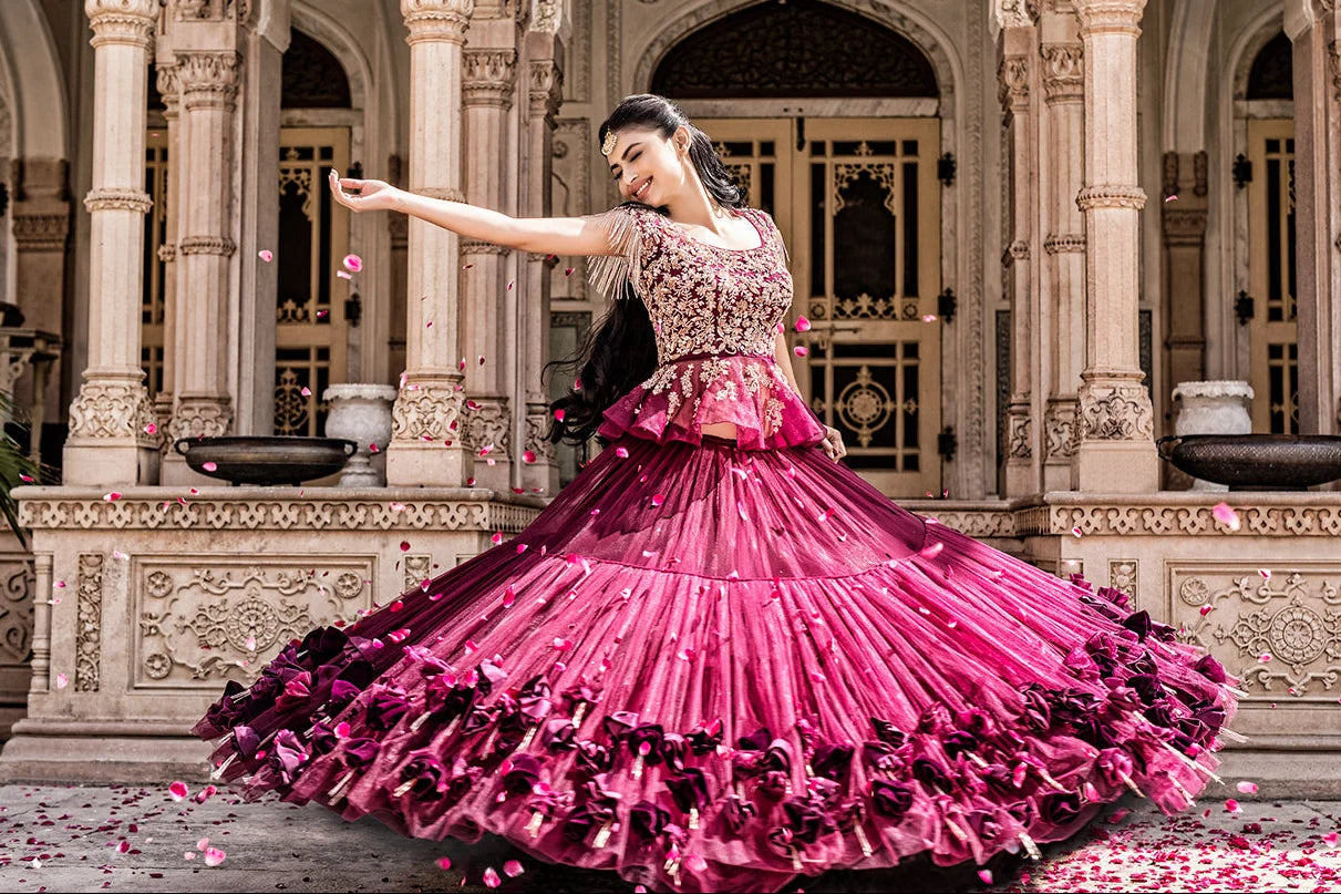 mouni roy in a pink and black traditional outfit dancing in an ornate indoor setting.