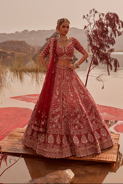 Woman in a red traditional outfit standing on a platform over water with a scenic background.