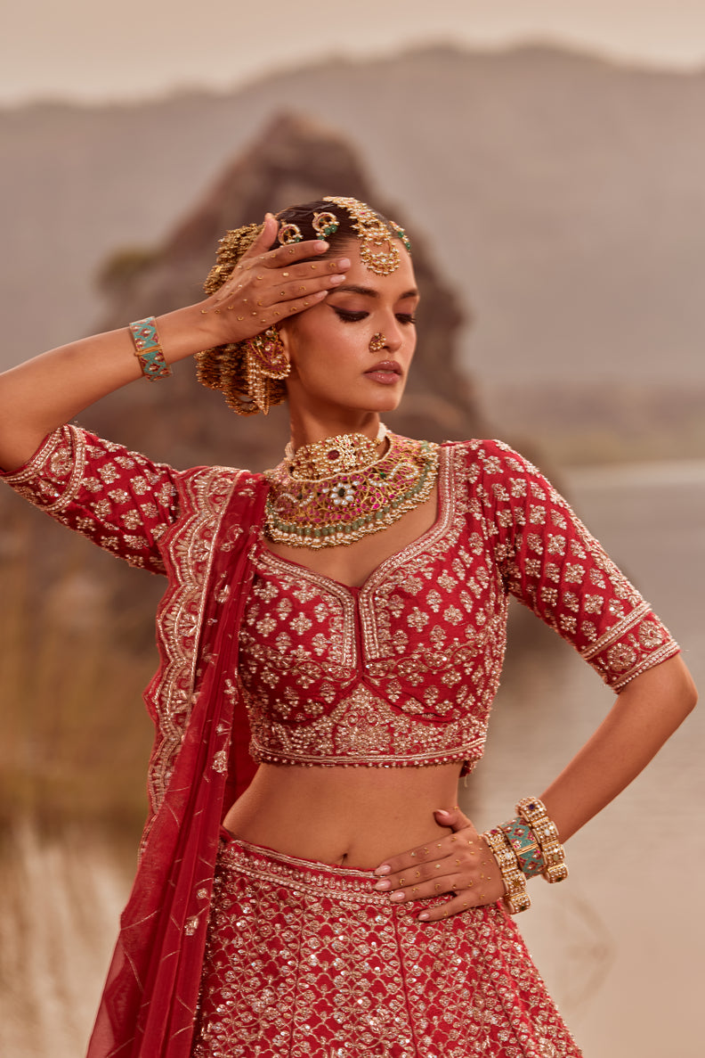 Woman in traditional red and white embroidered outfit with jewelry against a blurred natural background
