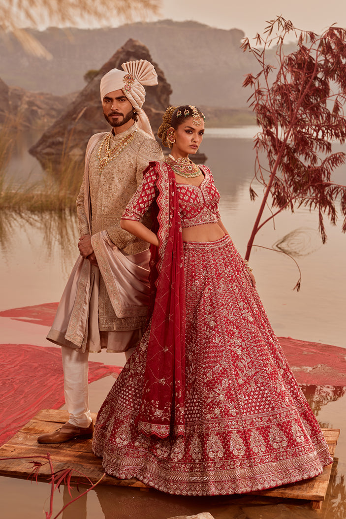 Man and woman in traditional attire standing by a lake with mountains in the background