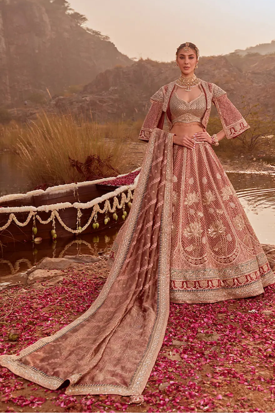 Woman in traditional pink embroidered outfit standing by a pond with mountains in the background