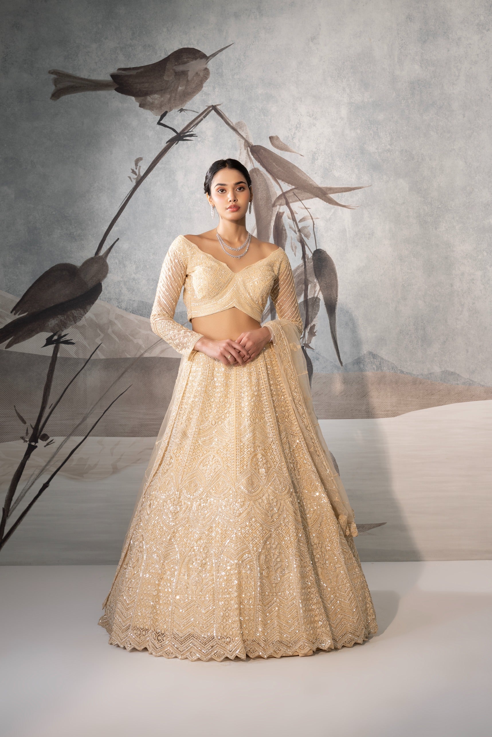 Woman in a gold traditional outfit standing against a textured wall with decorative birds.