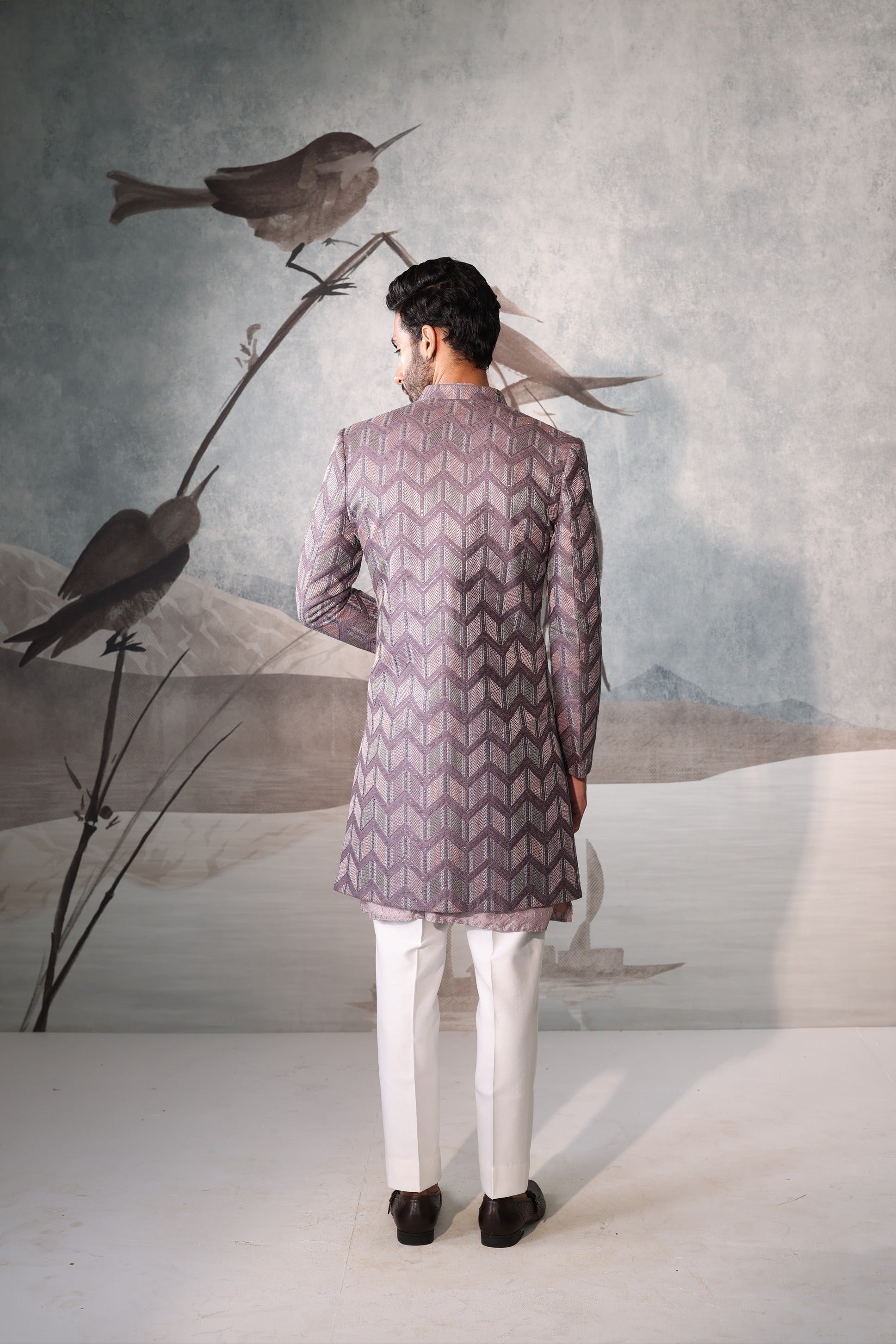 Man wearing a patterned kurta standing in front of a wall with birds and nature-themed decor.