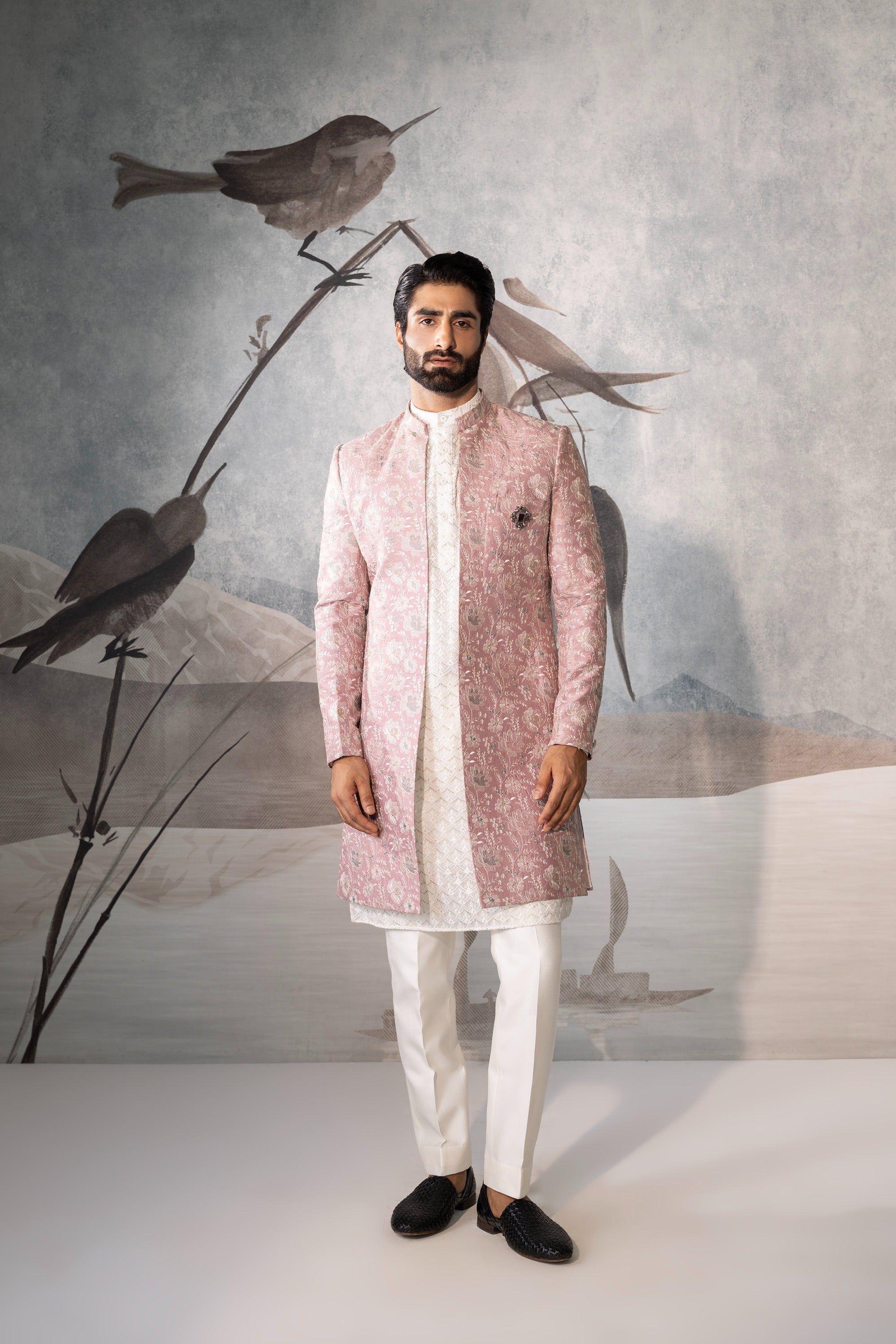 Man wearing a pink sherwani with white pants against a neutral background