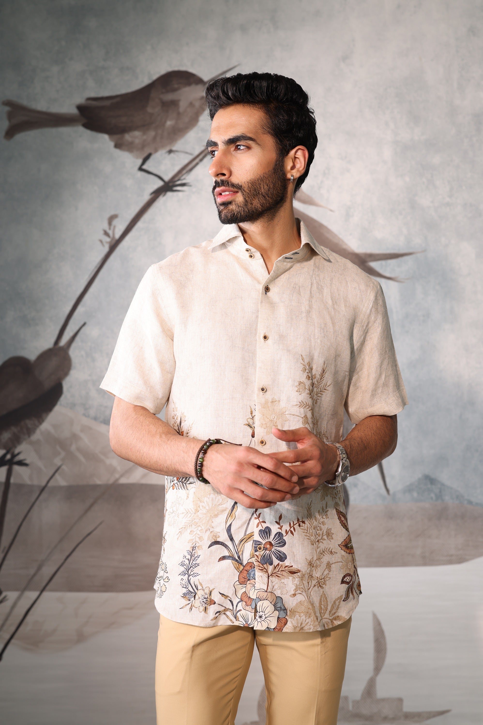 Man wearing a beige floral shirt and beige pants against a gray background with bird illustrations.