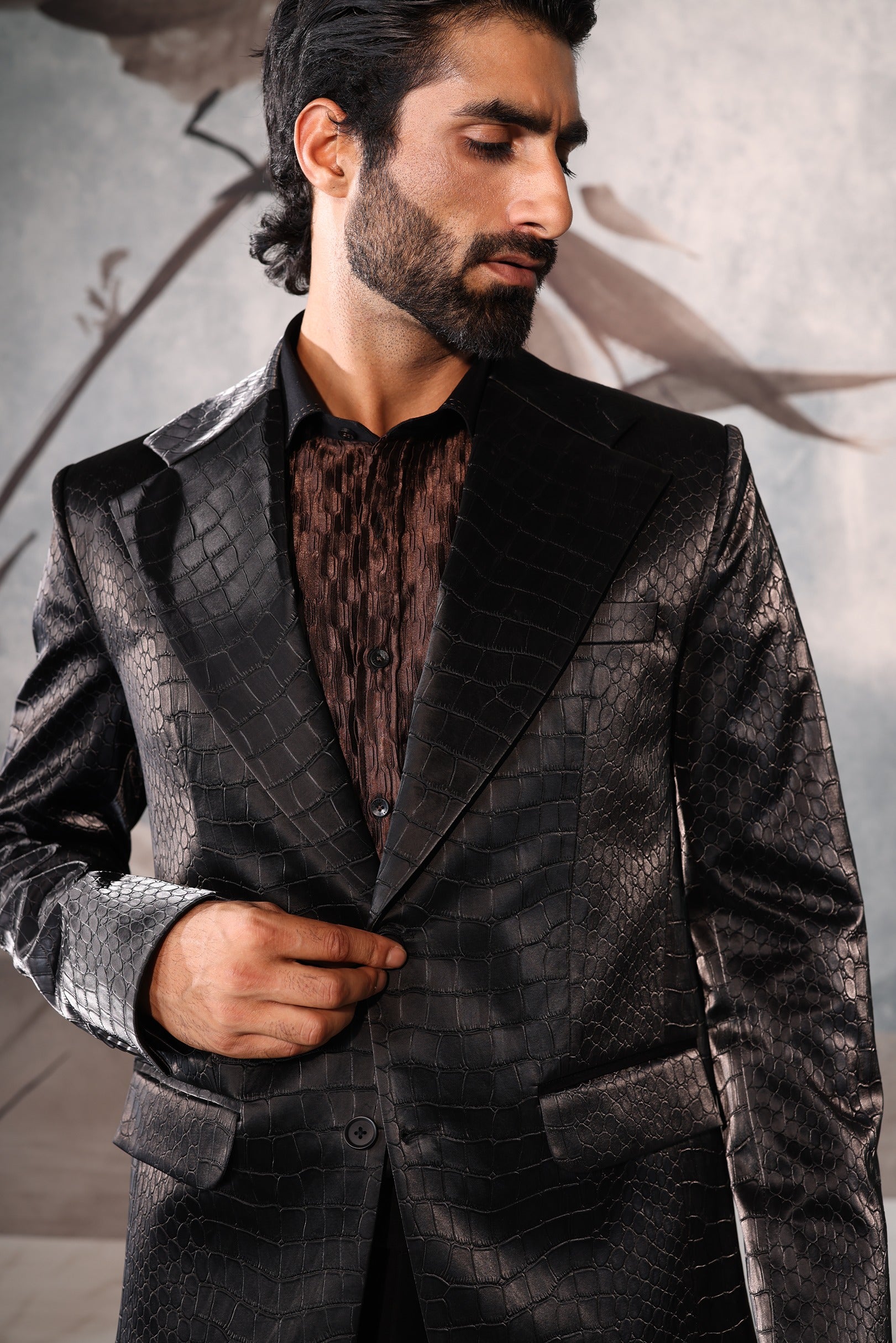 Man wearing a dark suit with a textured shirt against a neutral background