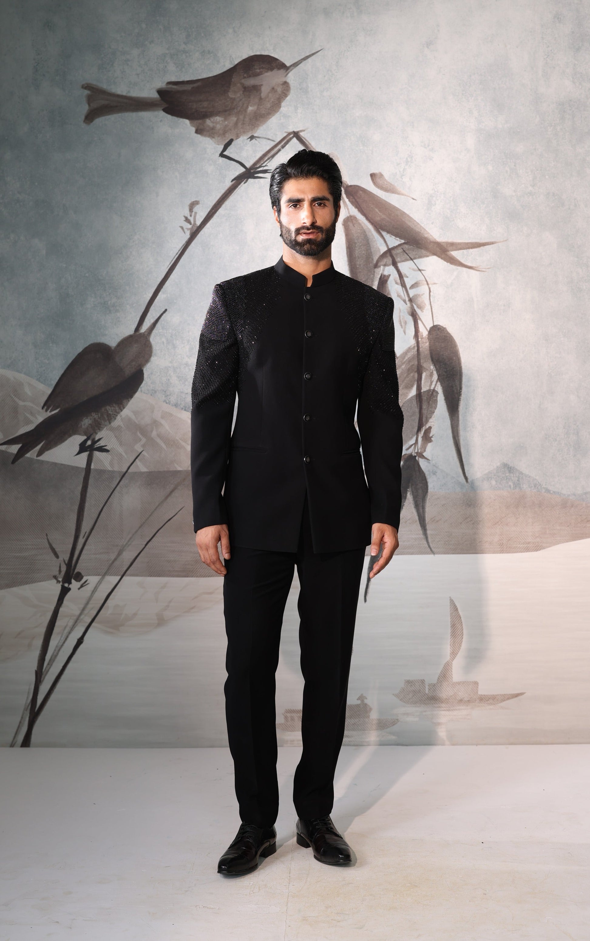 Man in a black suit standing in front of a wall with bird artwork