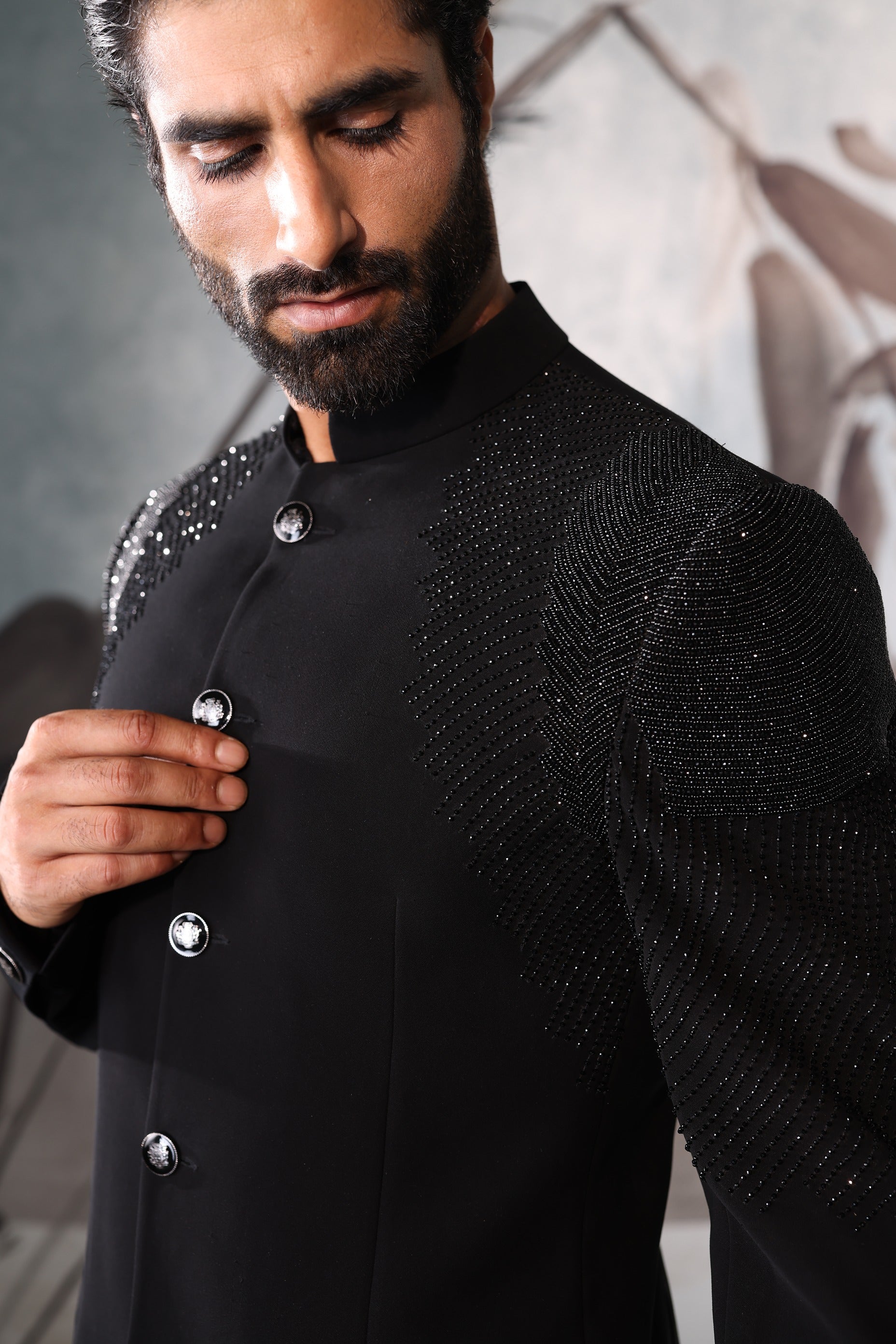 Man wearing a black embroidered traditional outfit with a blurred background