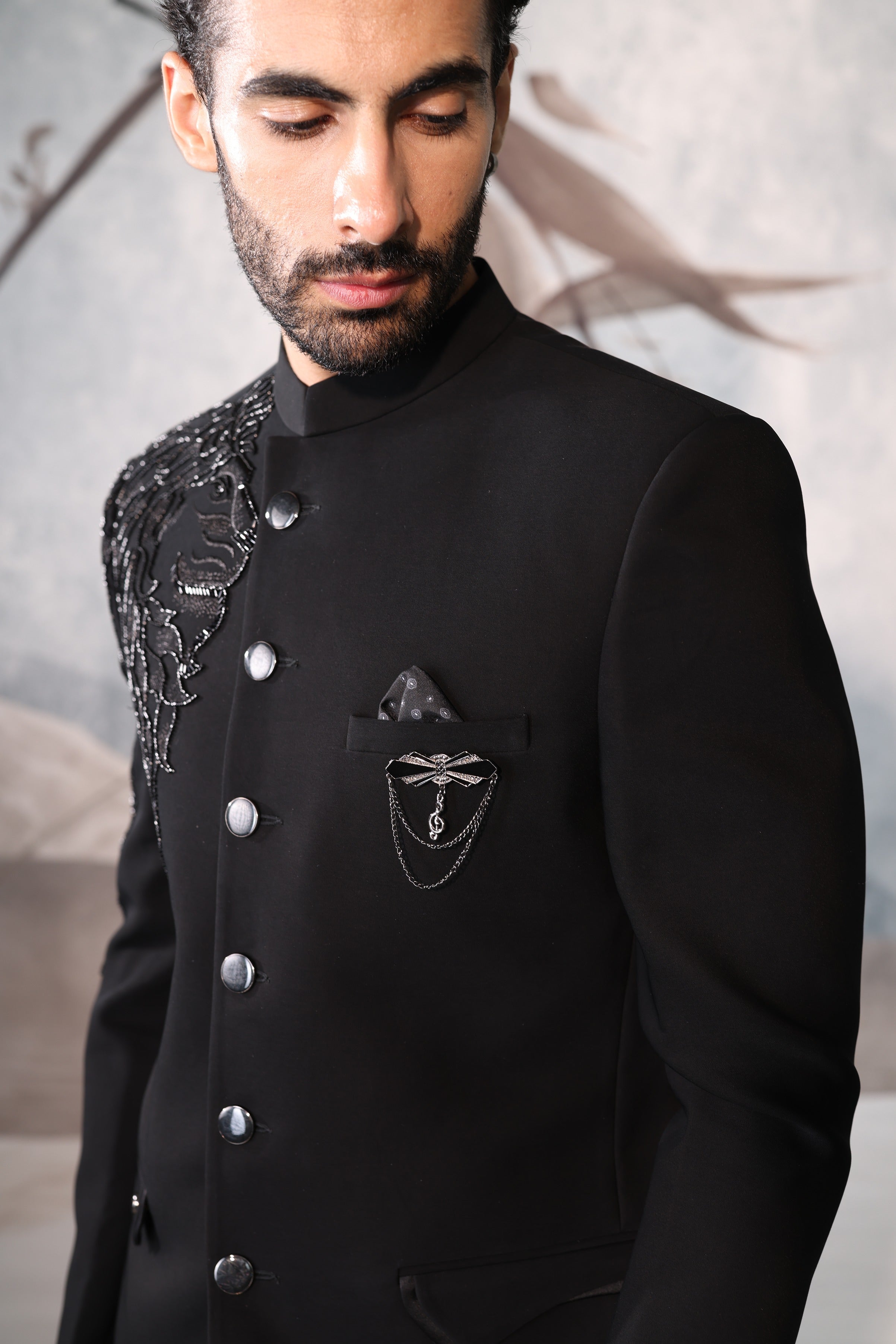 Man wearing a black coat with decorative elements against a neutral background