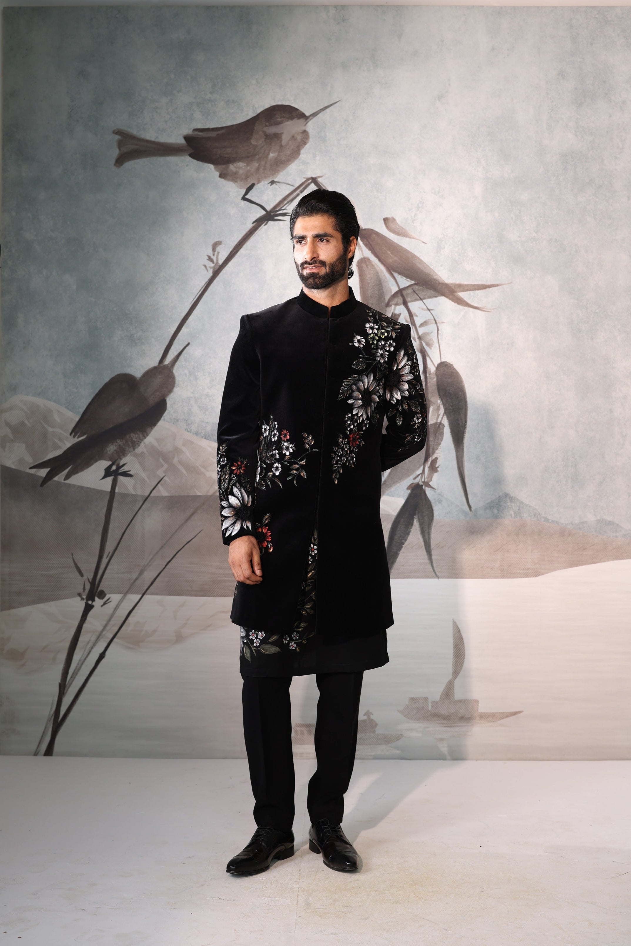 Man in a black traditional outfit standing in front of a wall with bird artwork