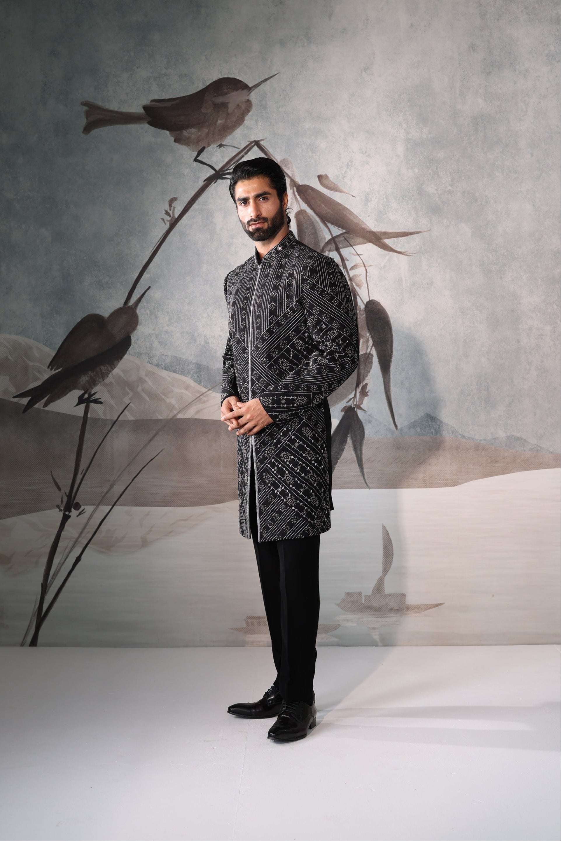 Man in a patterned outfit standing in front of a decorative wall with birds.