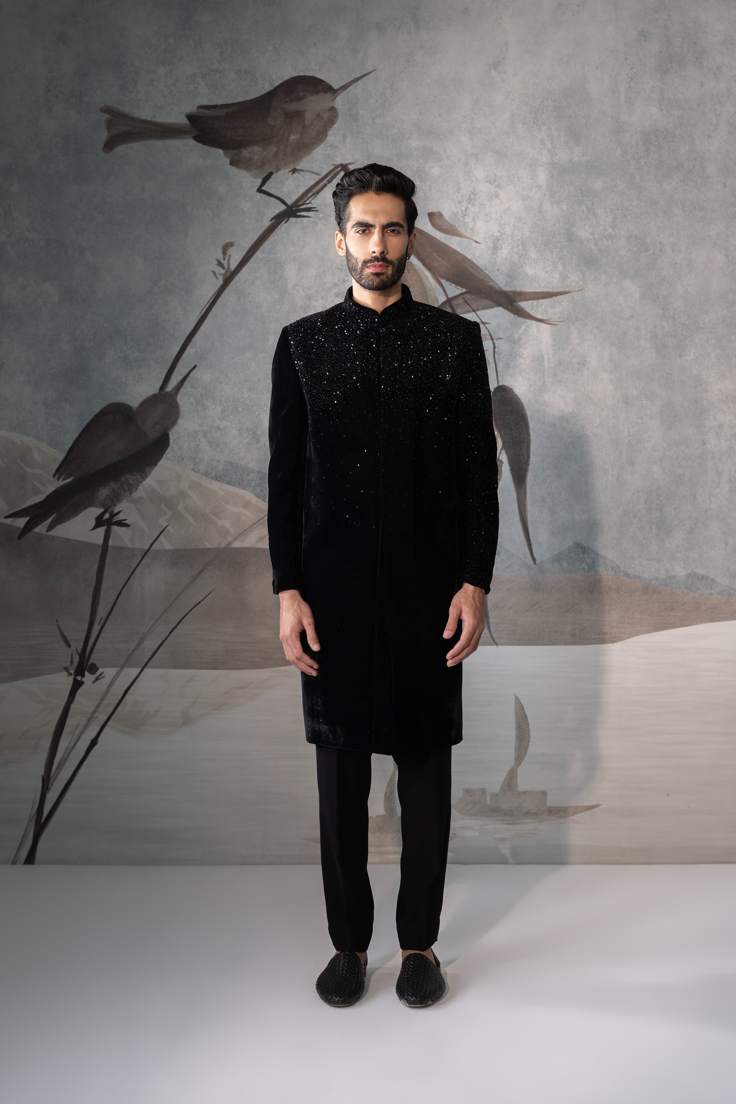 Man wearing a black traditional outfit with a stylized bird illustration in the background