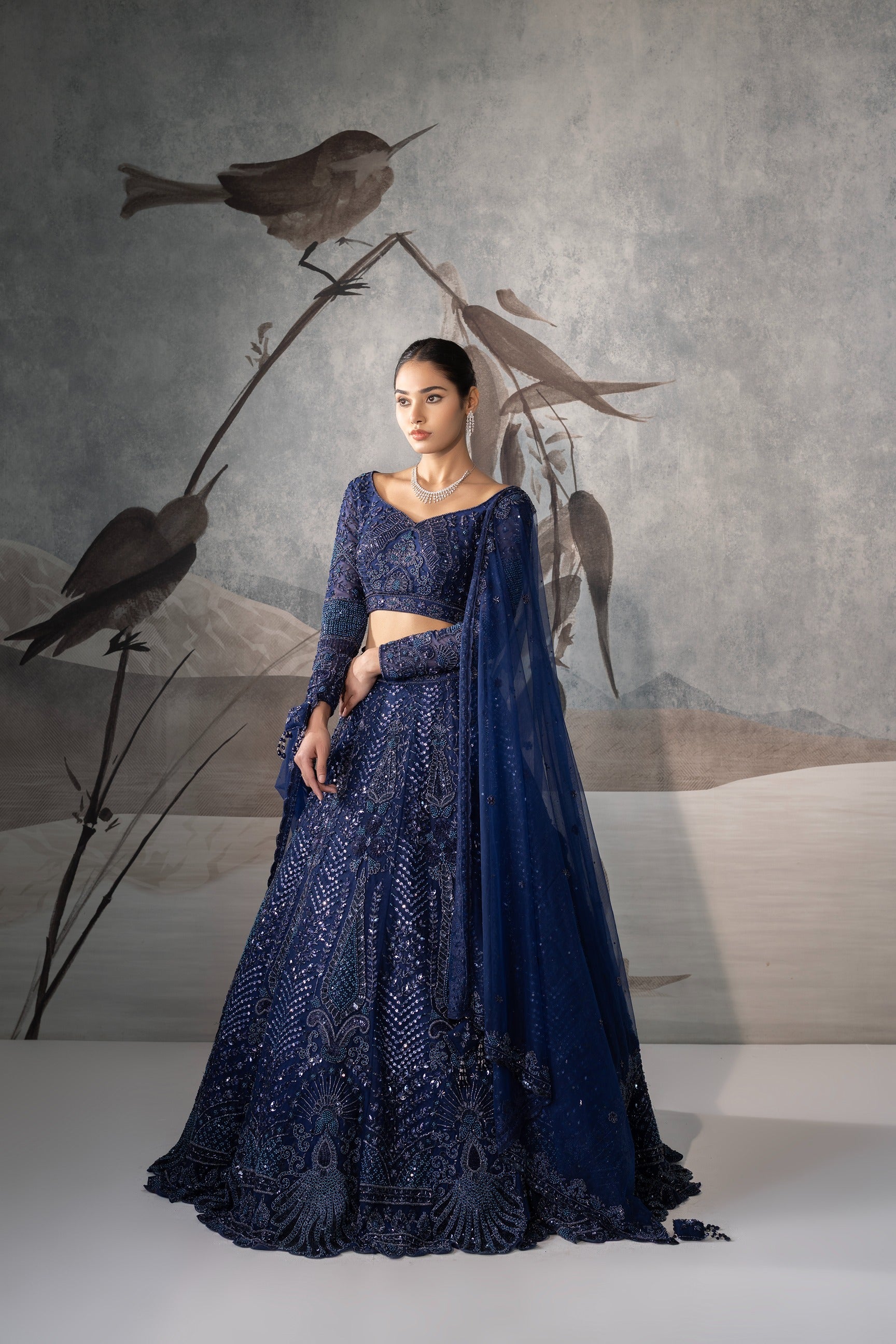 Woman in a blue embroidered outfit standing against a wall with bird artwork.
