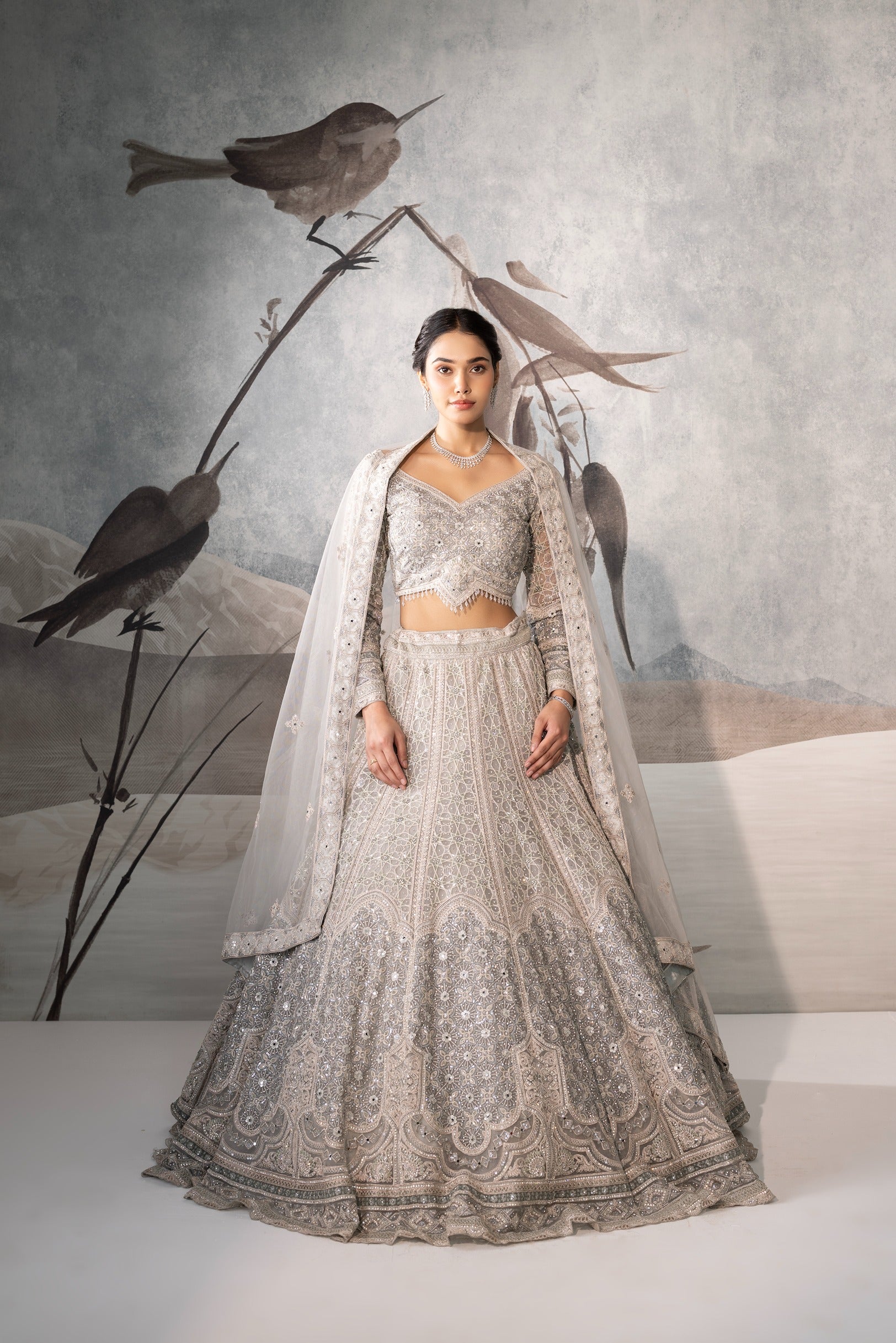 Woman in a silver embroidered lehenga with birds on a branch in the background