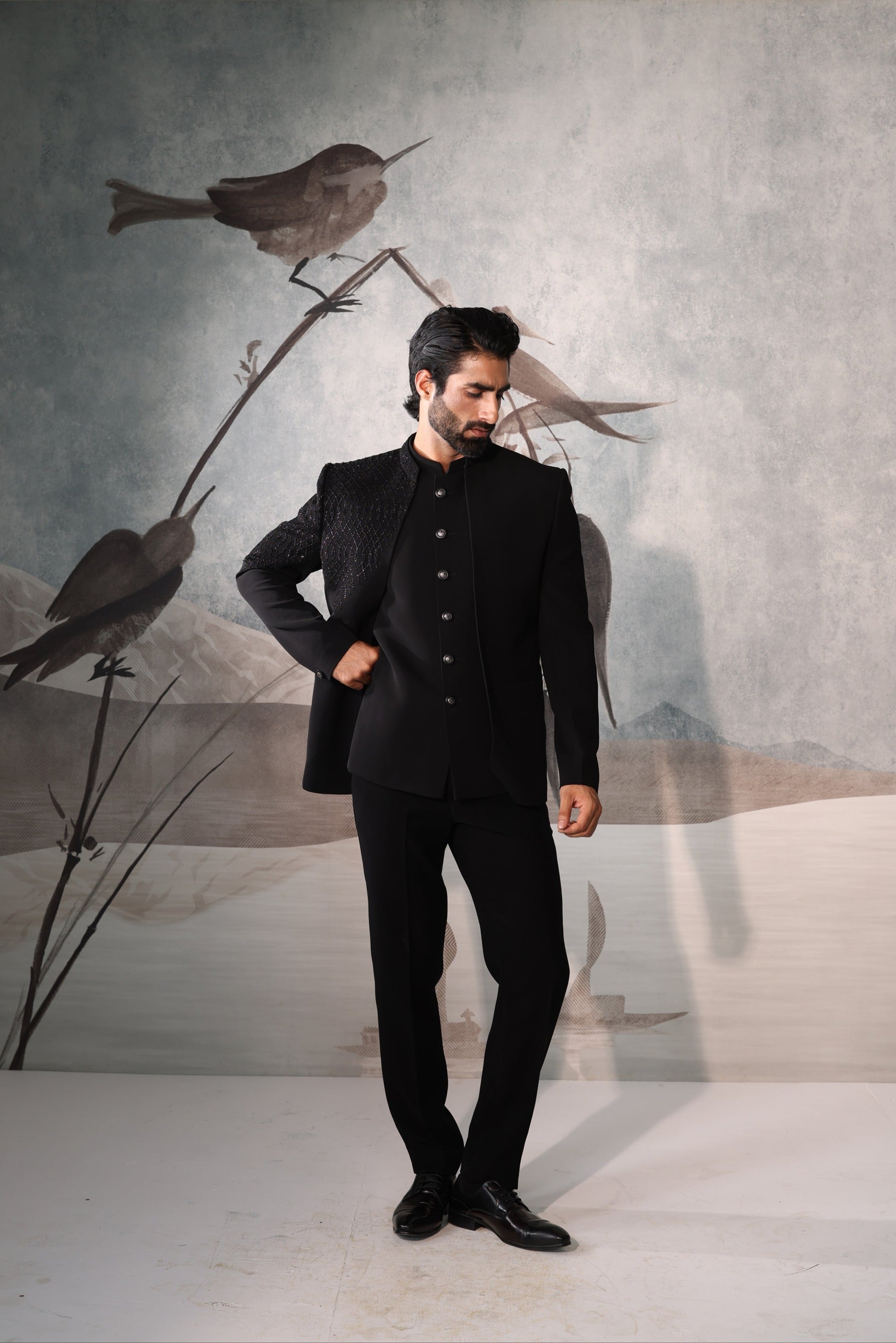 Man in a black suit standing in front of a wall with bird illustrations