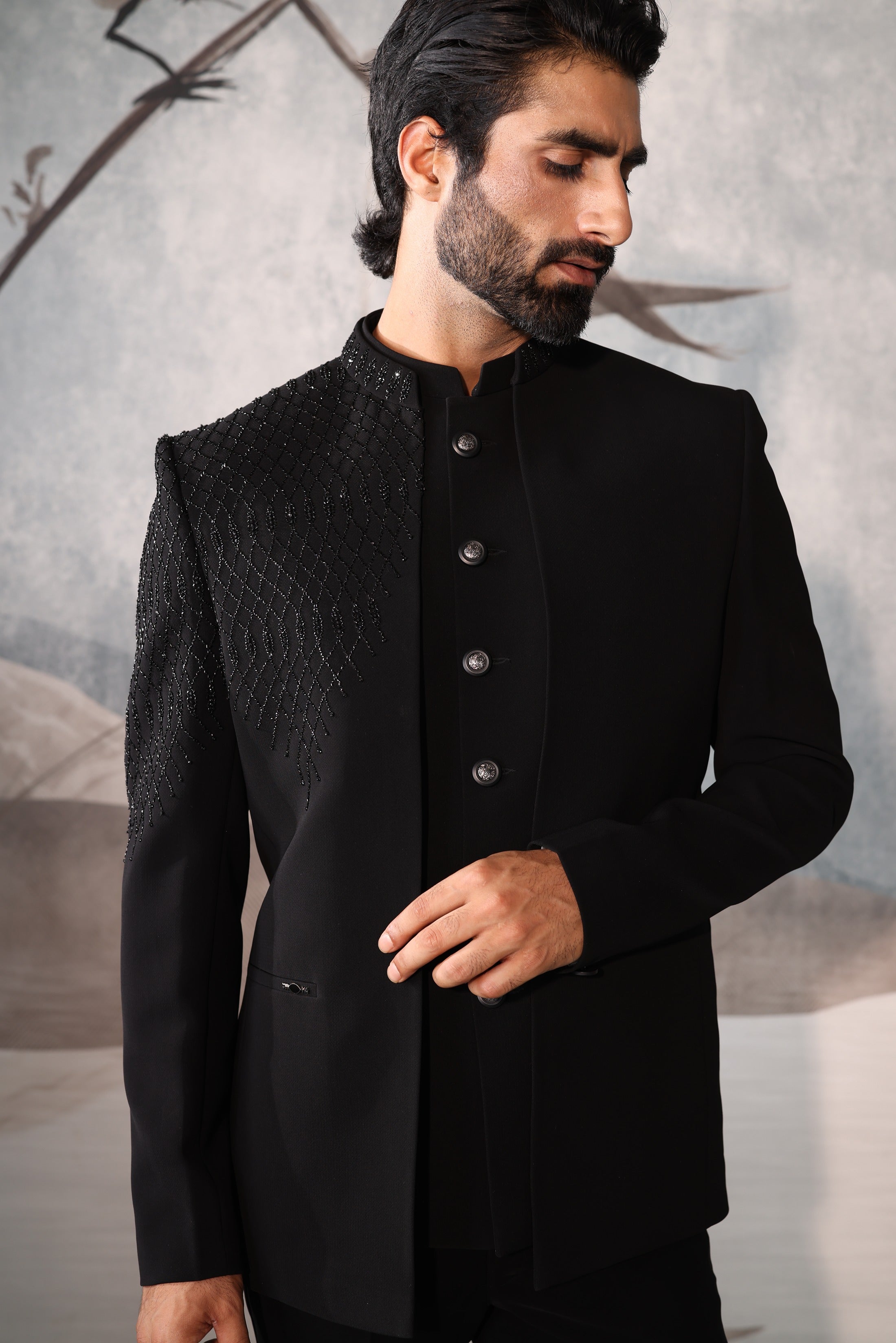 Man wearing a black traditional outfit against a neutral background