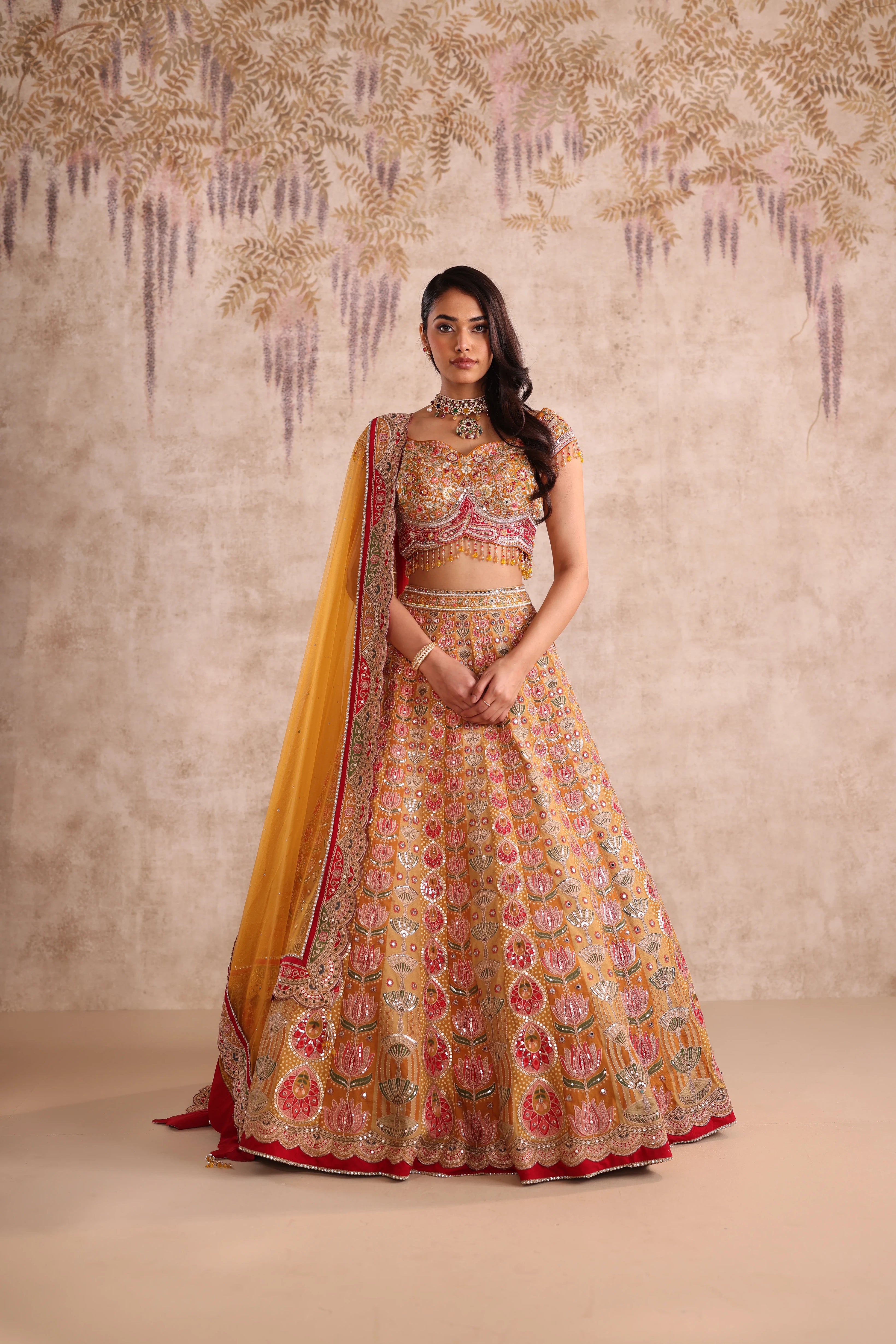 Woman in a traditional embroidered lehenga with a yellow dupatta against a neutral background