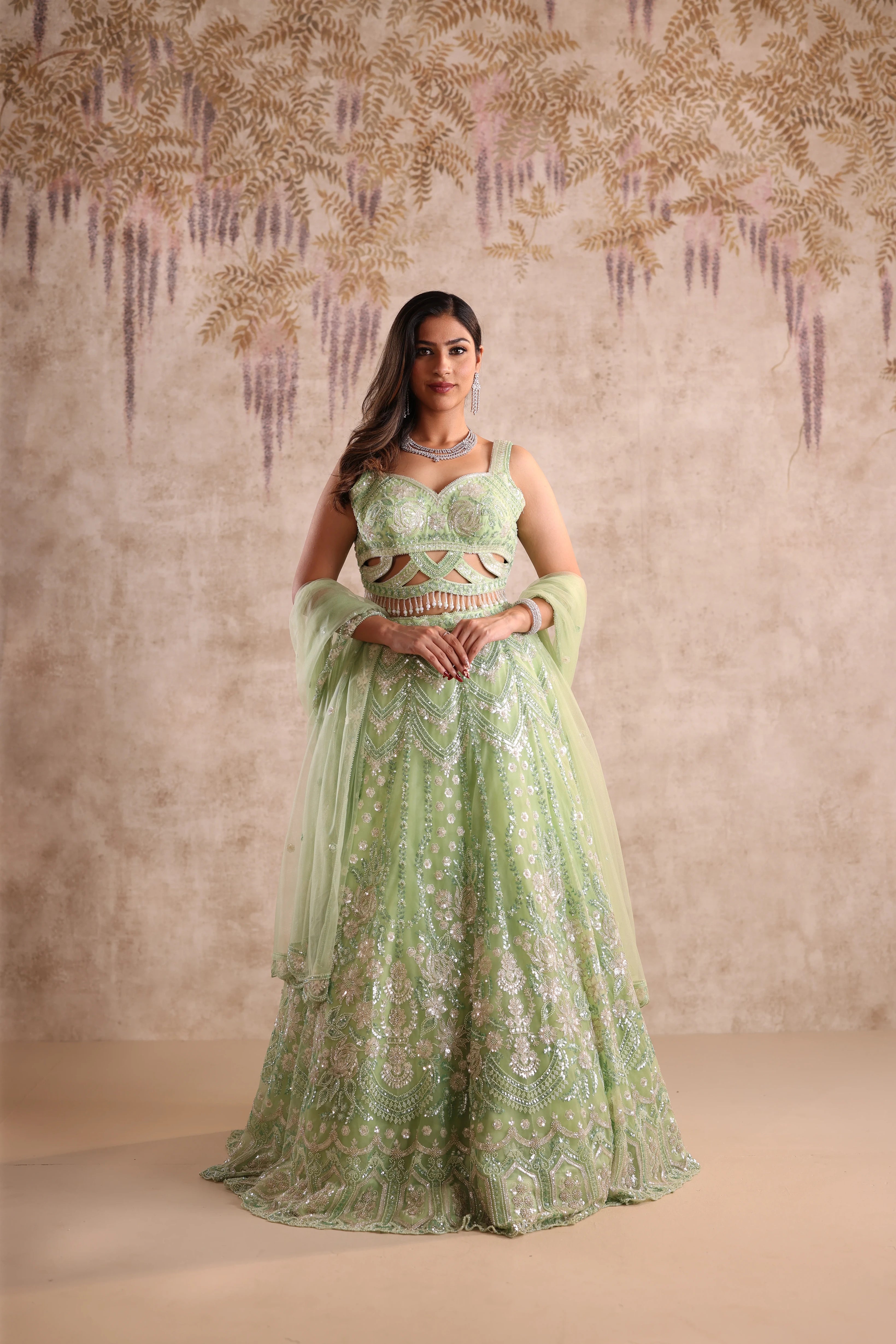 Woman in a green embroidered dress standing against a decorative wall.