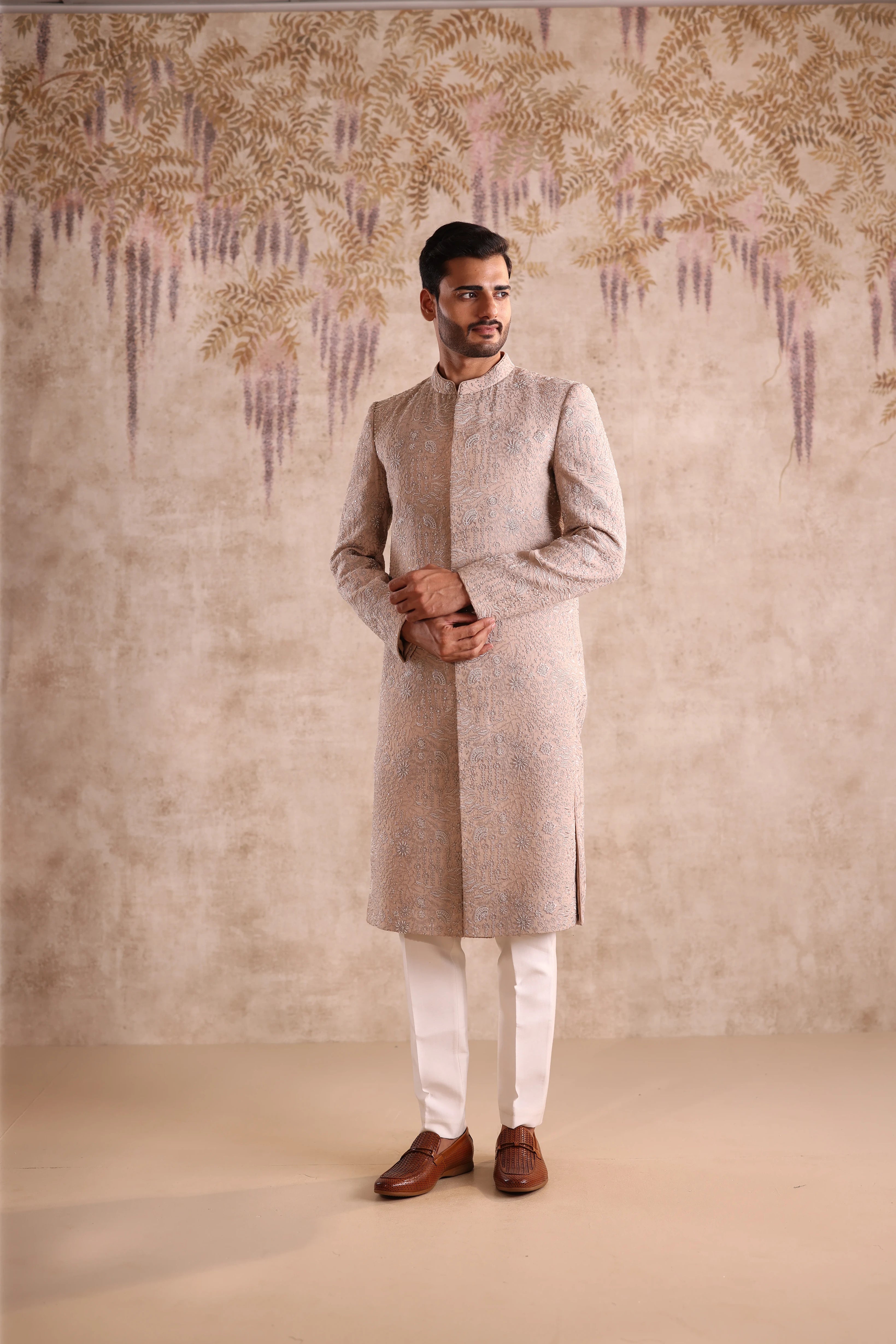 Man wearing a traditional kurta with a decorative wall in the background
