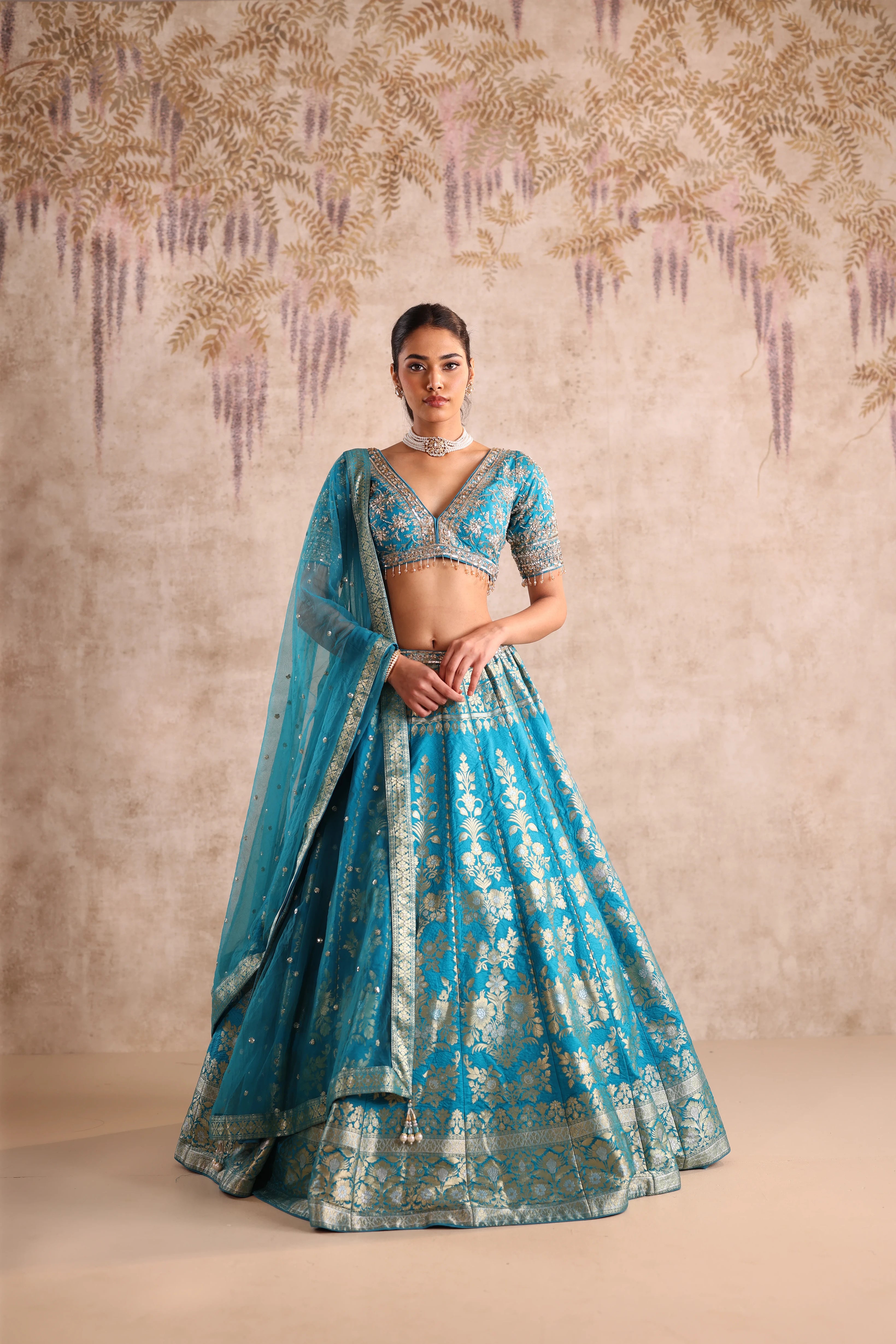 Woman wearing a blue traditional outfit with intricate patterns against a beige background