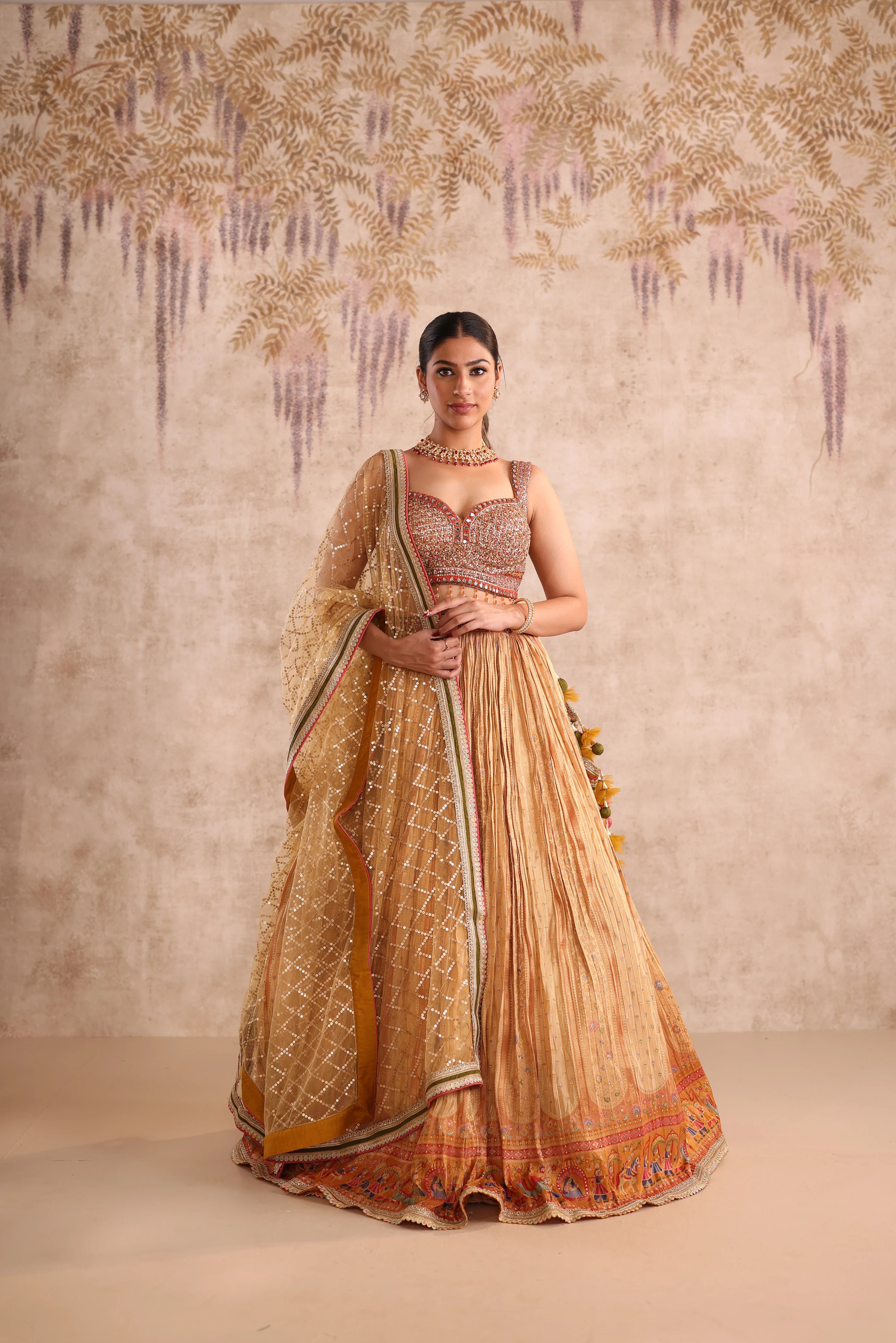 Woman wearing a traditional beige and orange saree with intricate patterns against a neutral background