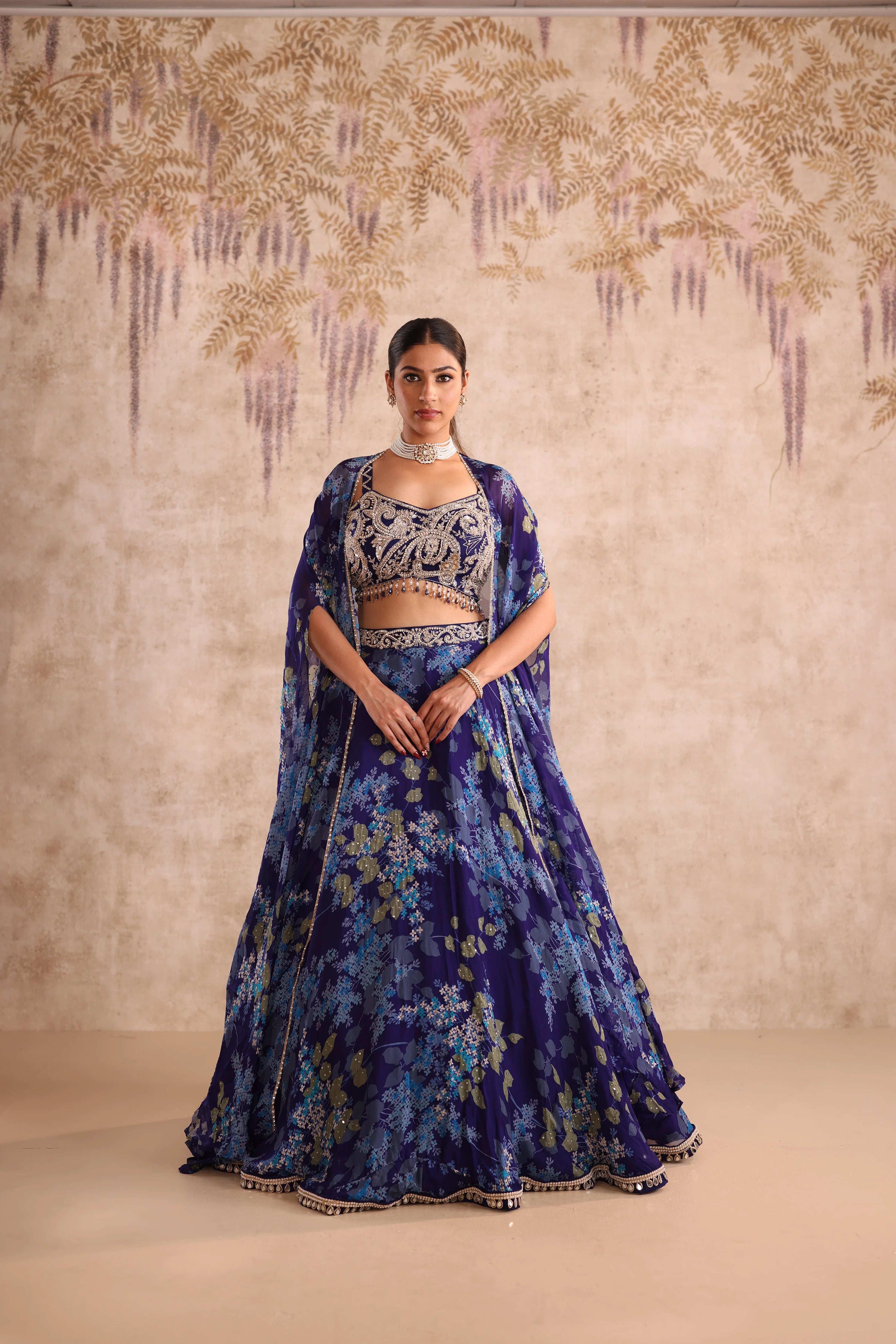 Woman wearing a blue floral traditional outfit against a decorative wall.
