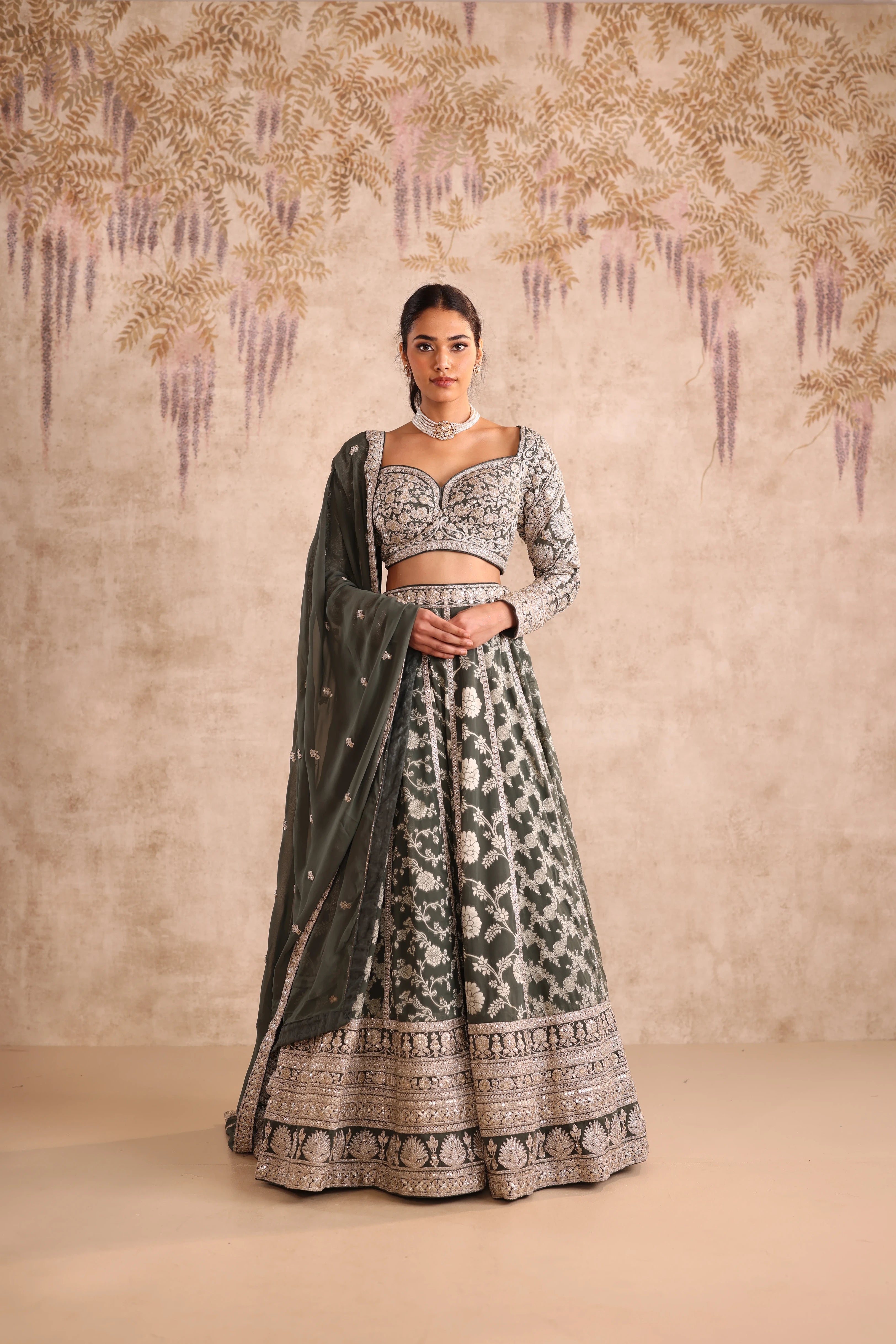 Woman in a traditional outfit with intricate patterns against a decorative wall.