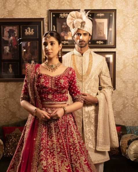 Traditional Indian couple in formal attire standing in a decorated room.