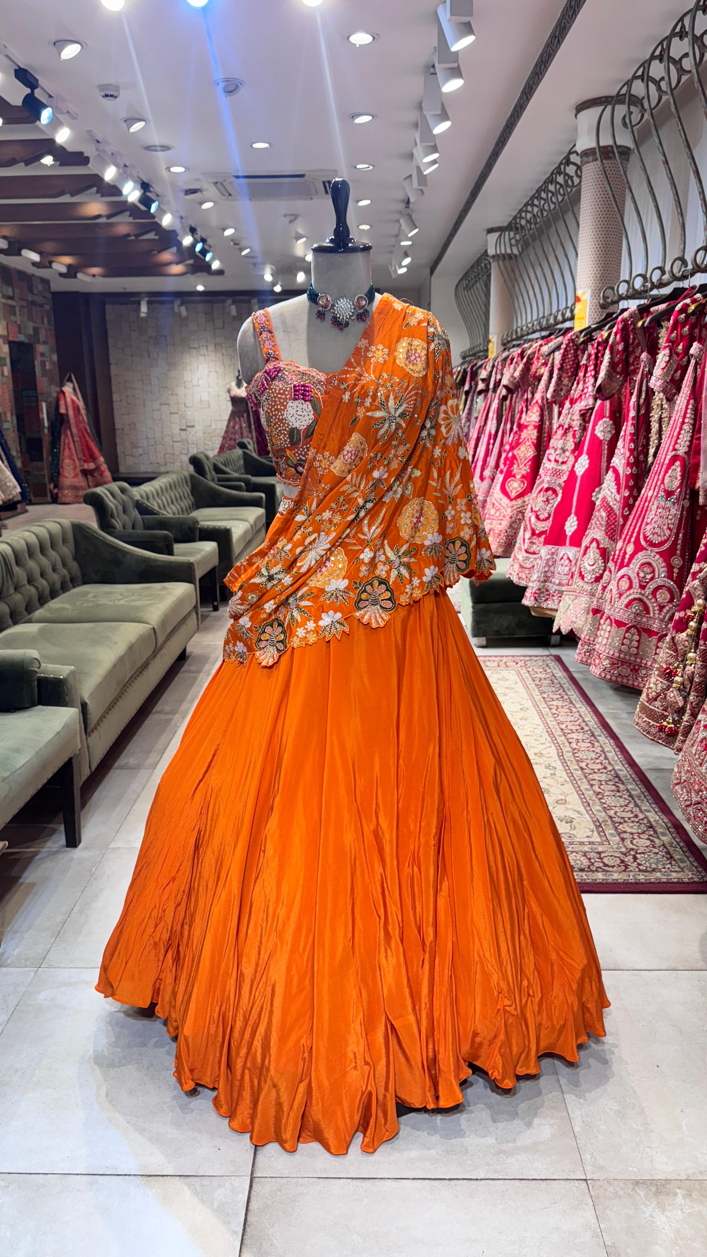 Orange traditional outfit on a mannequin in a store setting with other dresses in the background.